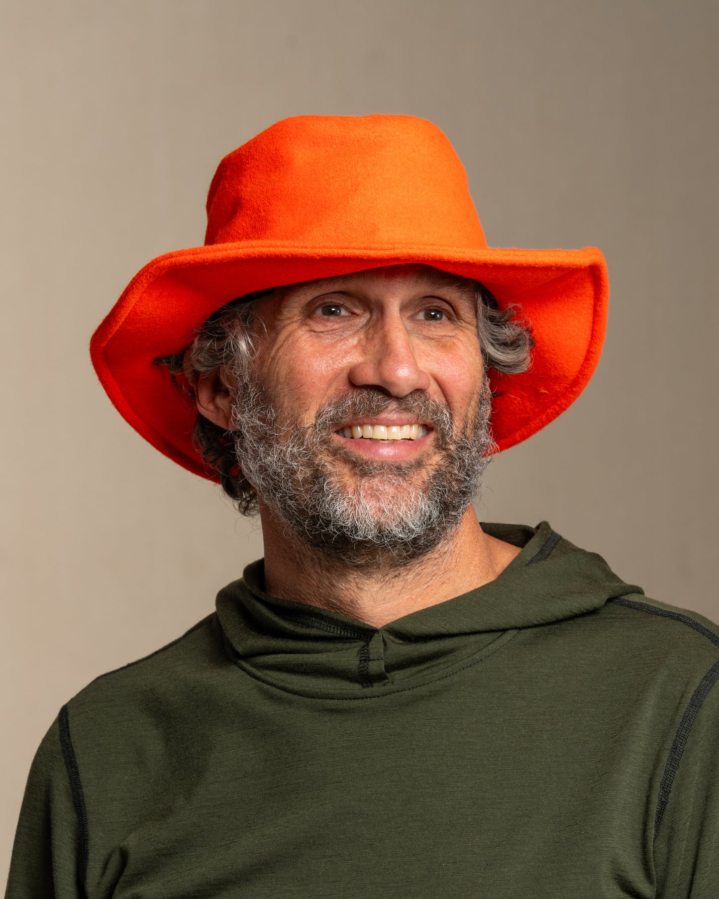 Man wearing a blaze orange crusher hat and green merino wool hoodie against a canvas background