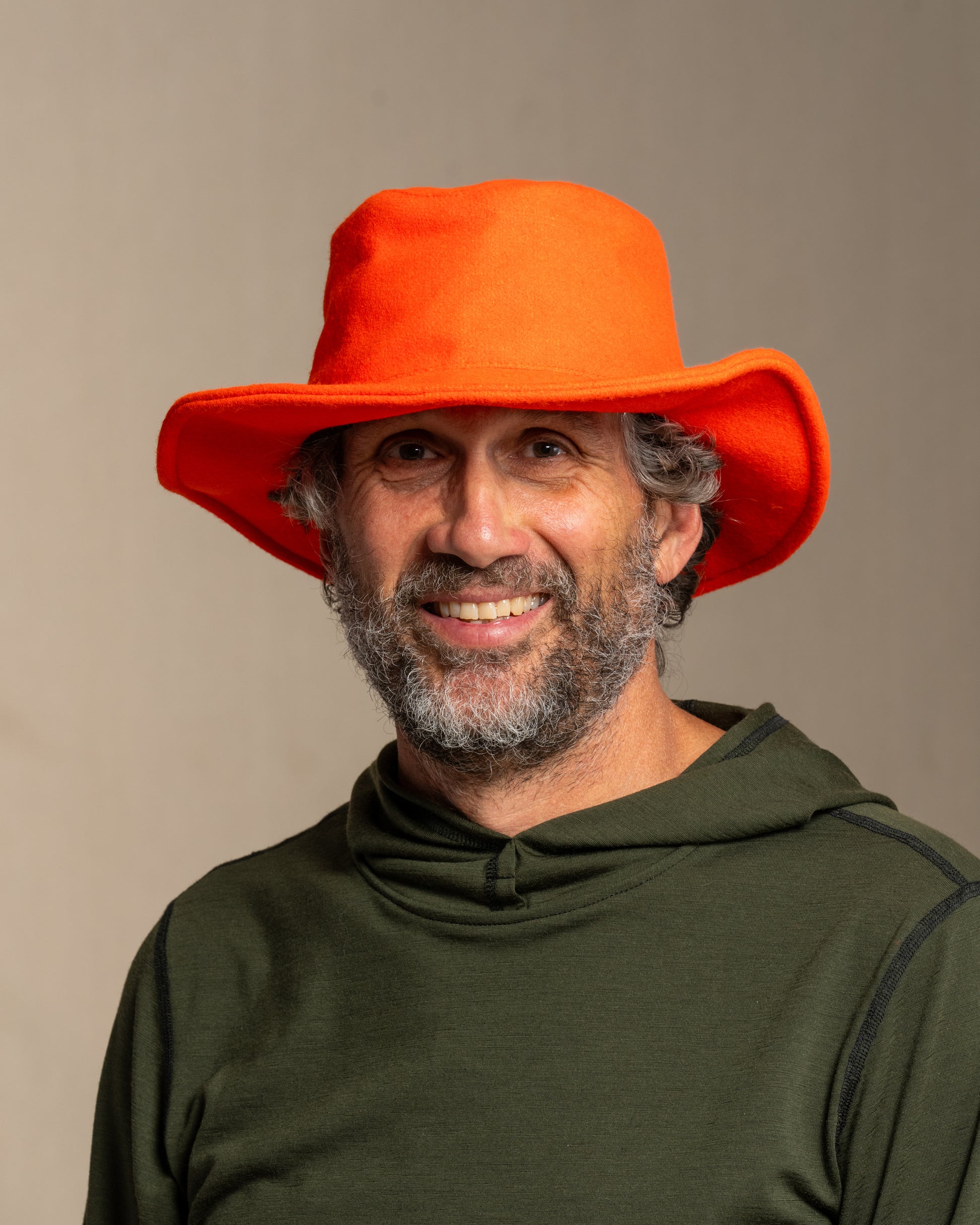 Person wearing a beagle blaze orange crusher hat and green merino wool hoodie against a canvas background