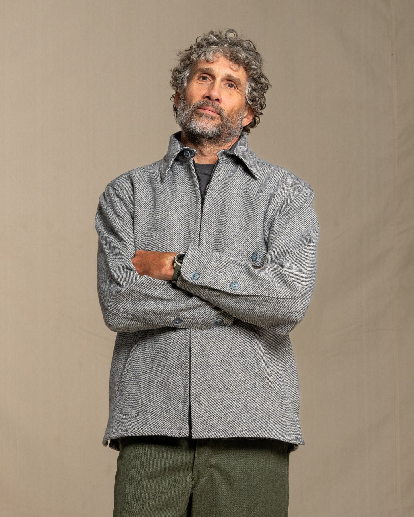 Man wearing a gray twill wool jacket and green pants standing against a plain background