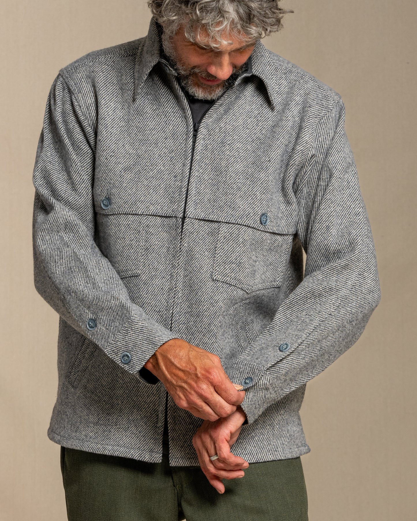 Man wearing a gray twill wool jacket and green pants standing against a plain background