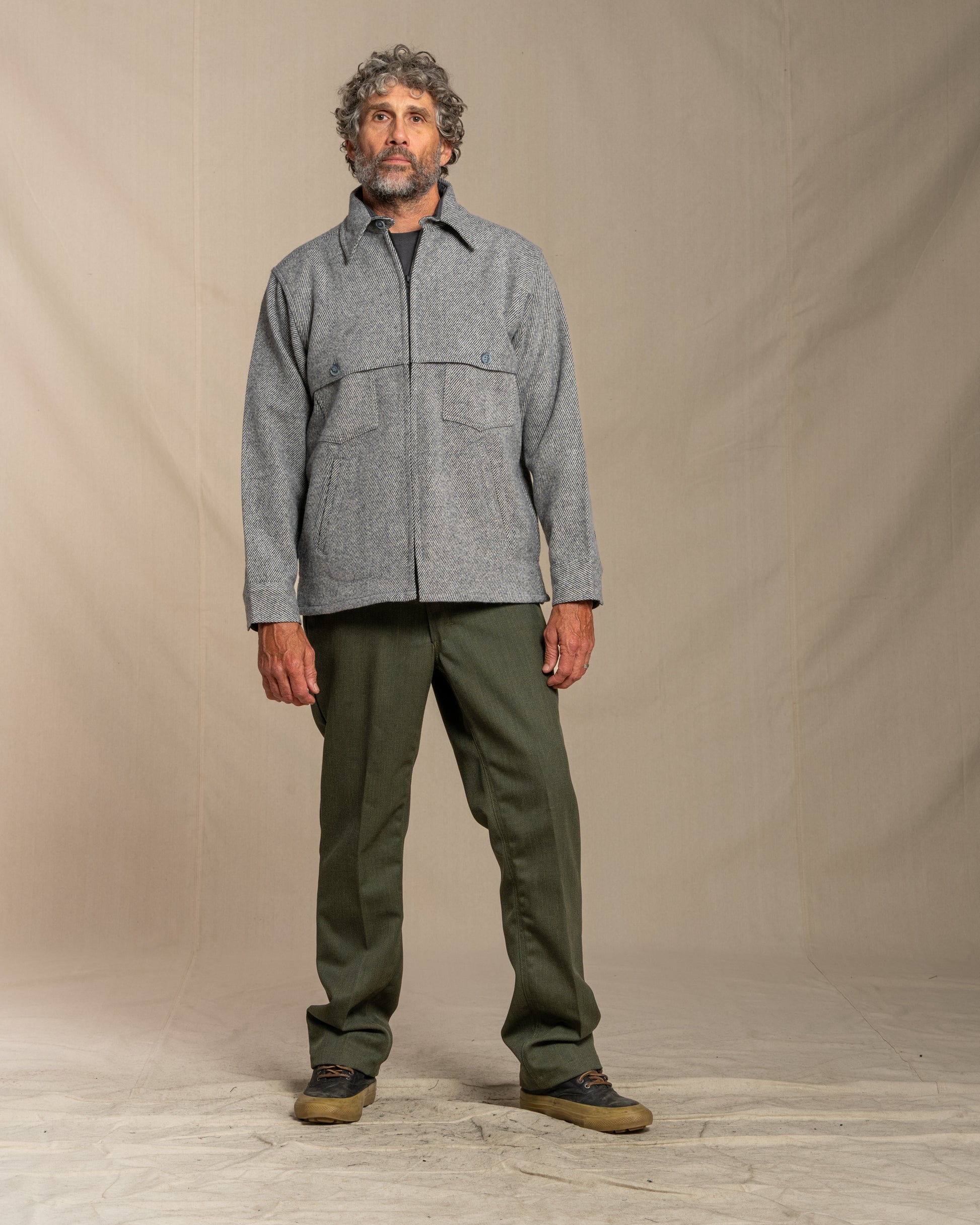 Man wearing a gray twill wool jacket and green pants standing against a plain background