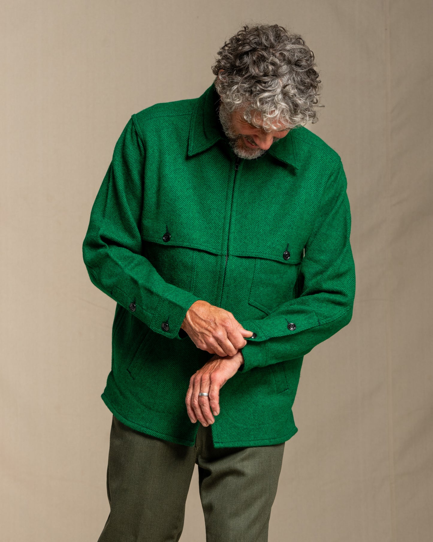 Man wearing a green twill wool jacket against a beige background