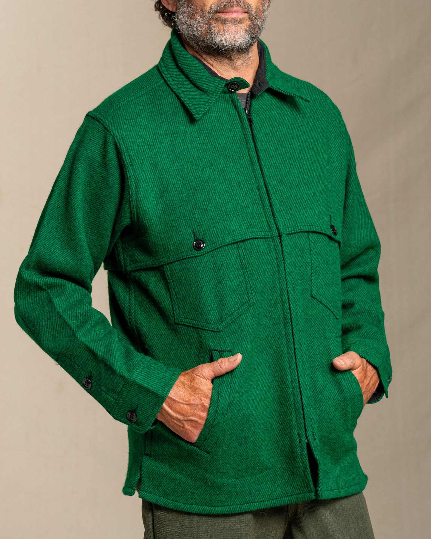 Man wearing a green twill wool jacket against a beige background