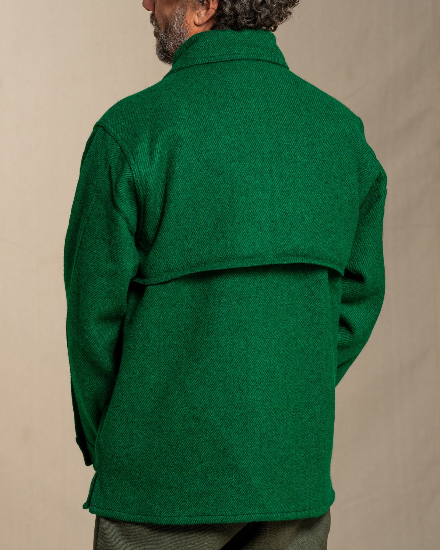 Man wearing a green twill wool jacket against a beige background
