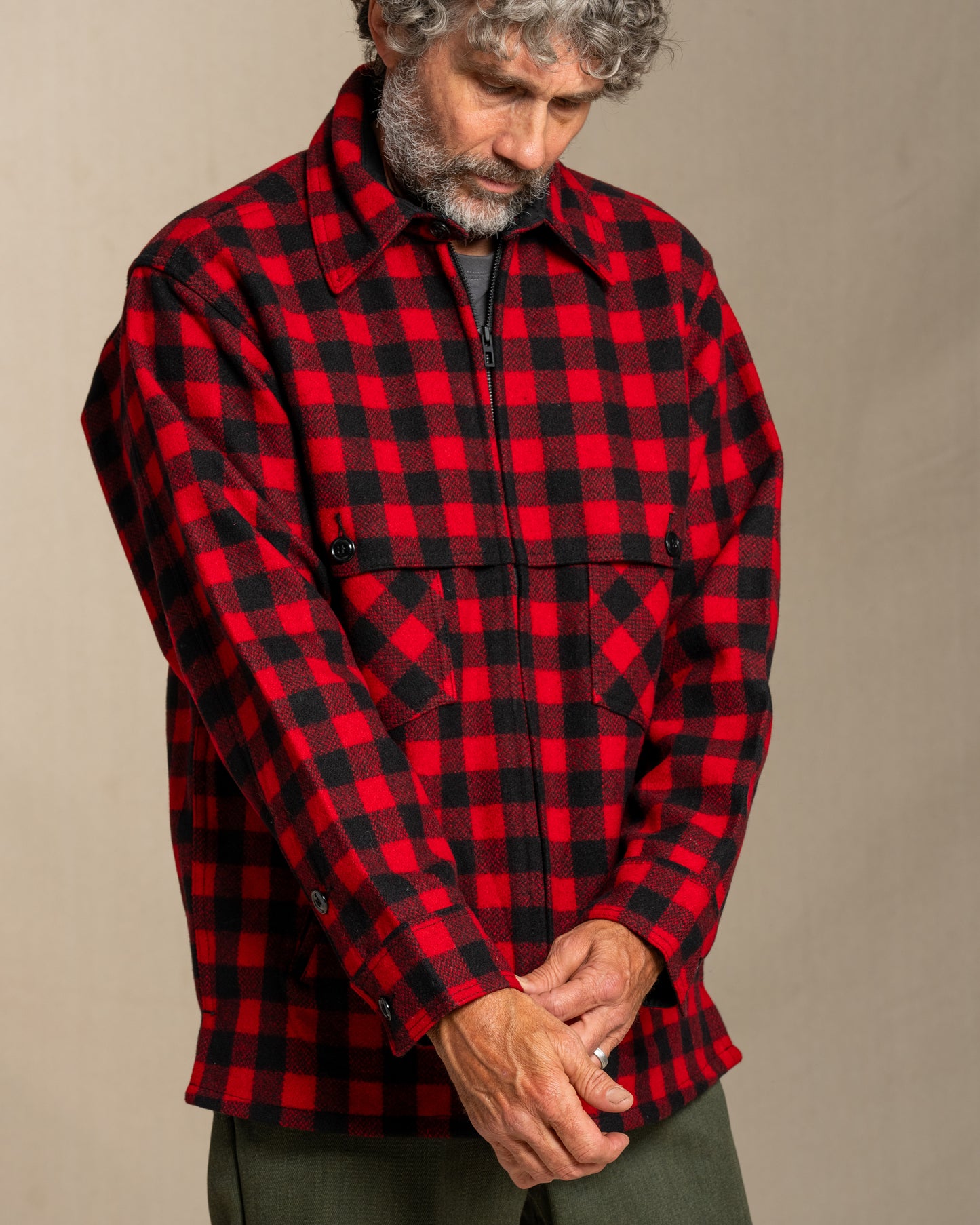 Man wearing a red and black wool checkered jacket against a beige background