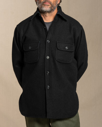 Man wearing a black wool shirt with two front pockets against a beige background