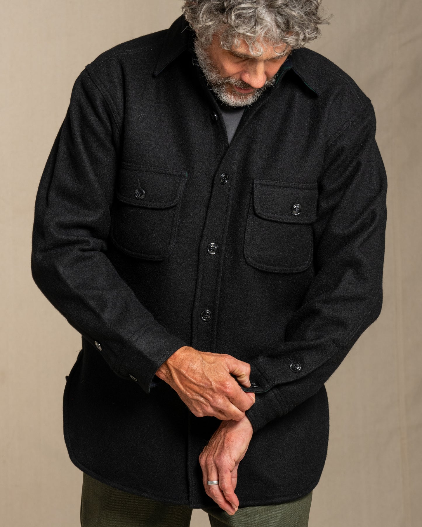 Man wearing a black wool shirt with pockets against a beige background