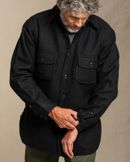 Man wearing a black wool shirt with pockets against a beige background