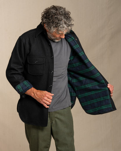 Man wearing a black wool shirt with plaid flannel lining, standing against a beige background