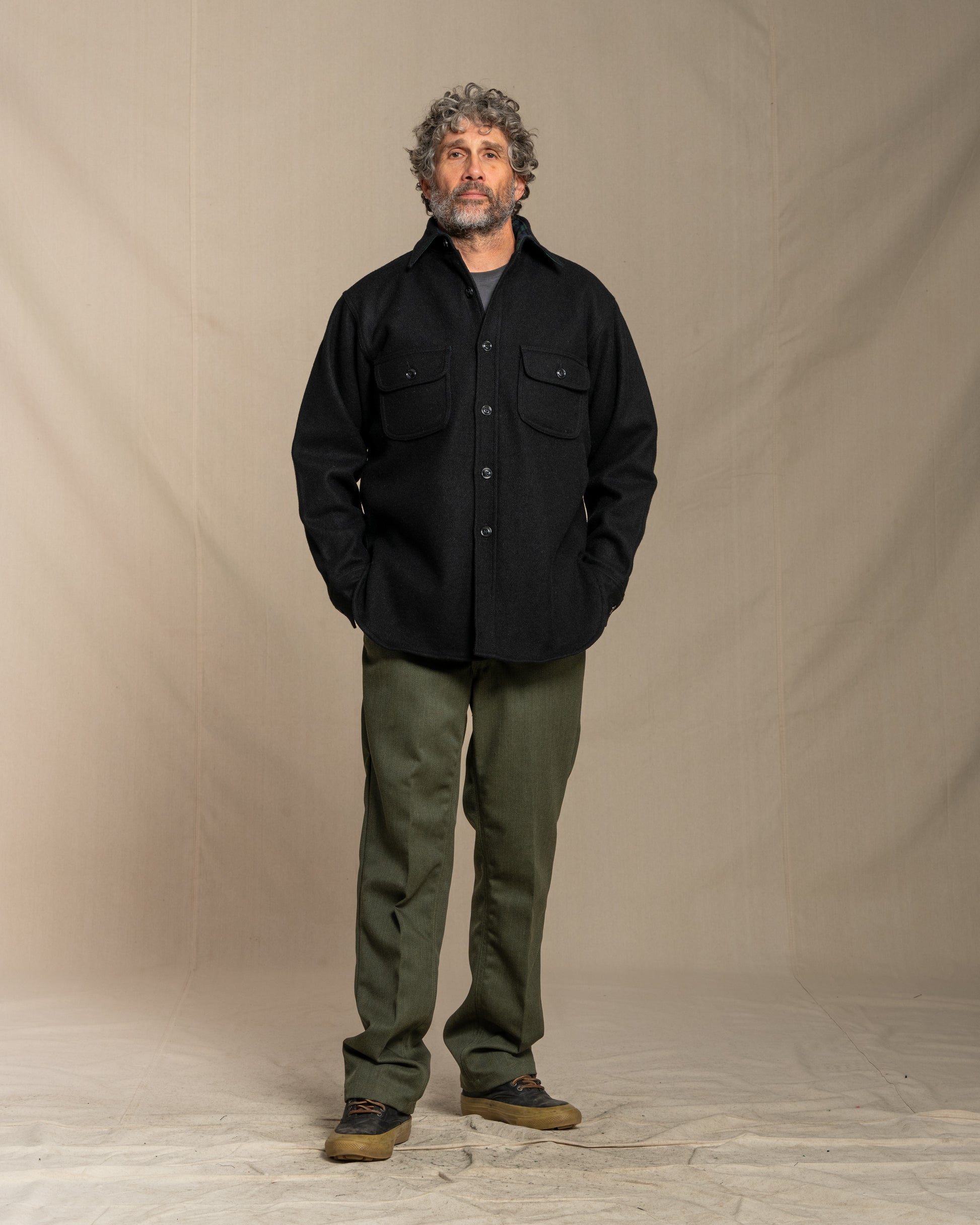 Man wearing a black wool shirt with pockets against a beige background