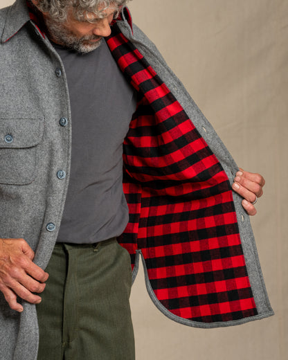 Person wearing a gray wool shirt with a red and black checkered flannel lining, standing against a canvas background.