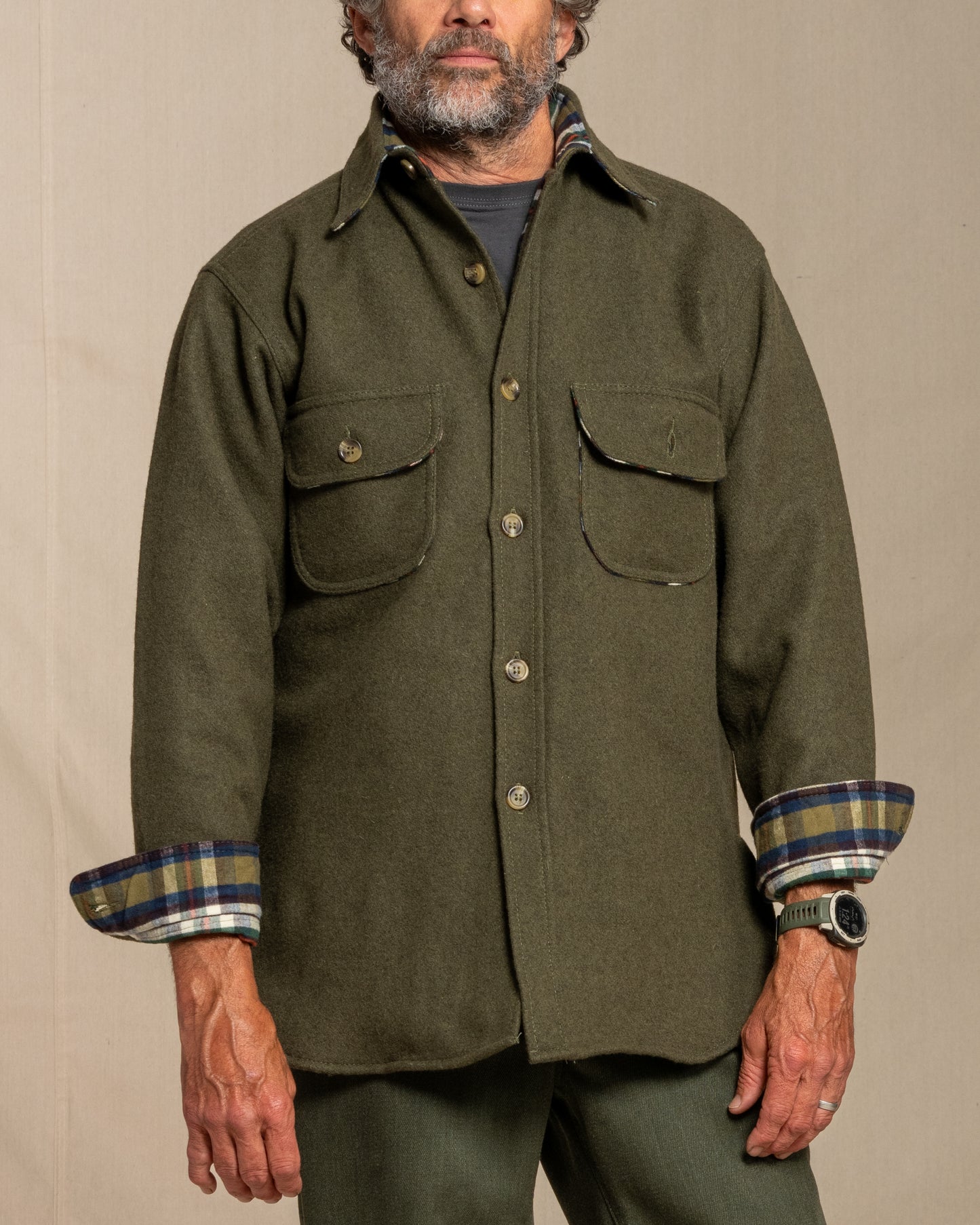 Man wearing a loden wool shirt with plaid cuffs against a beige background