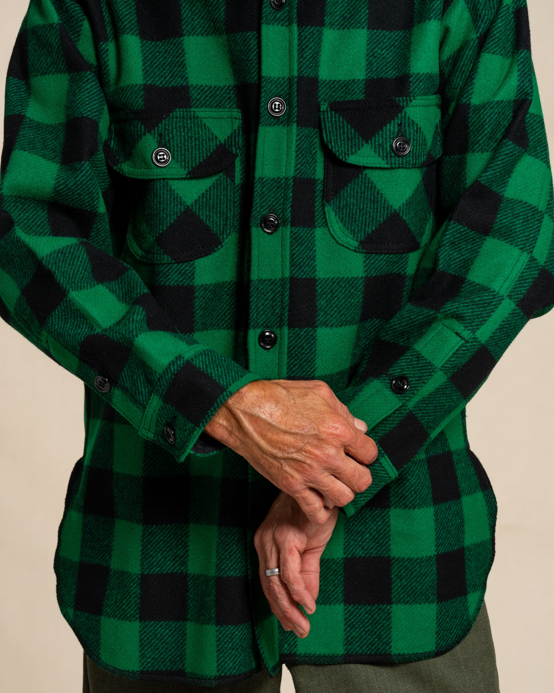 Man wearing a green and black checkered wool shirt against a beige background