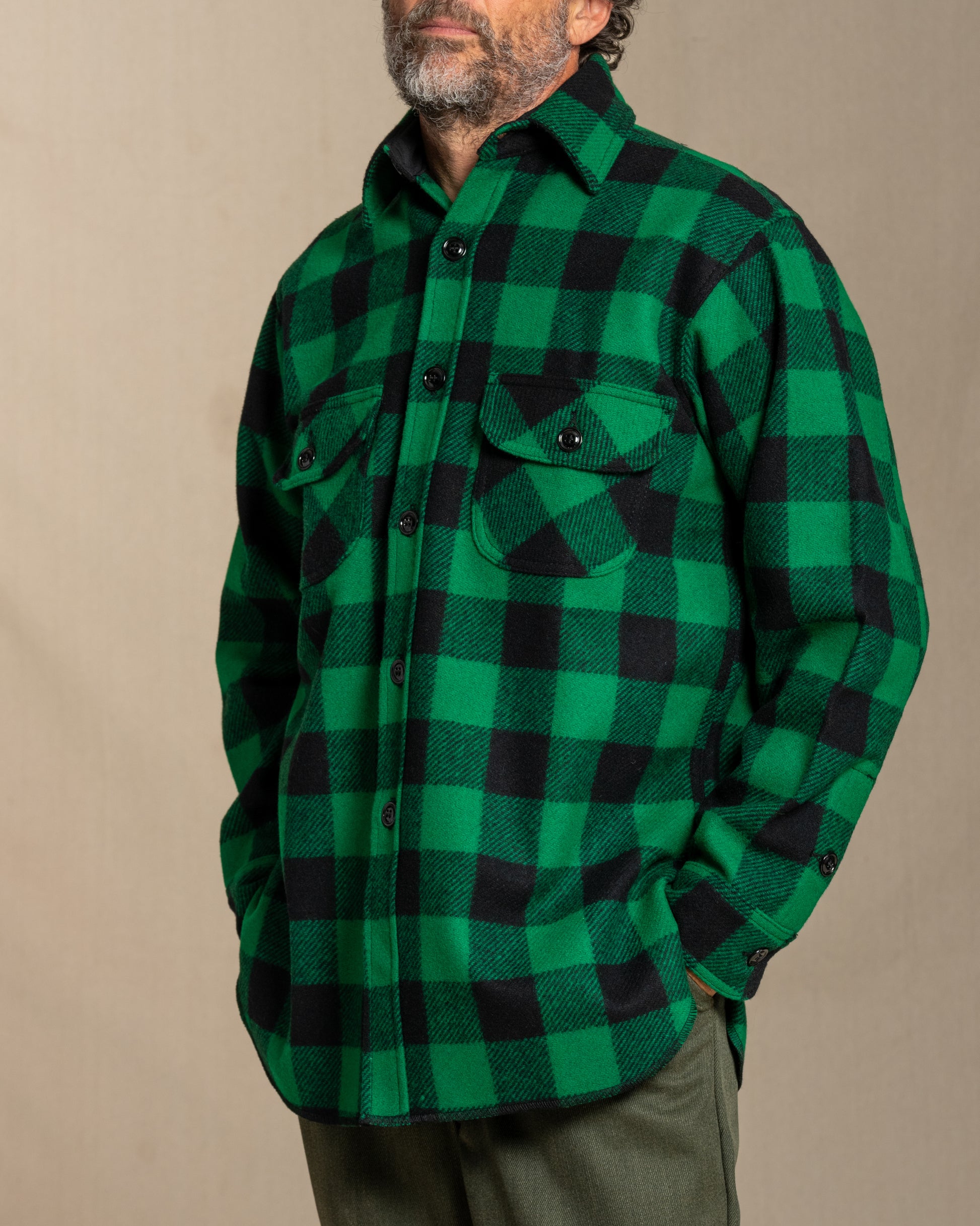 Man wearing a green and black checkered wool shirt against a beige background