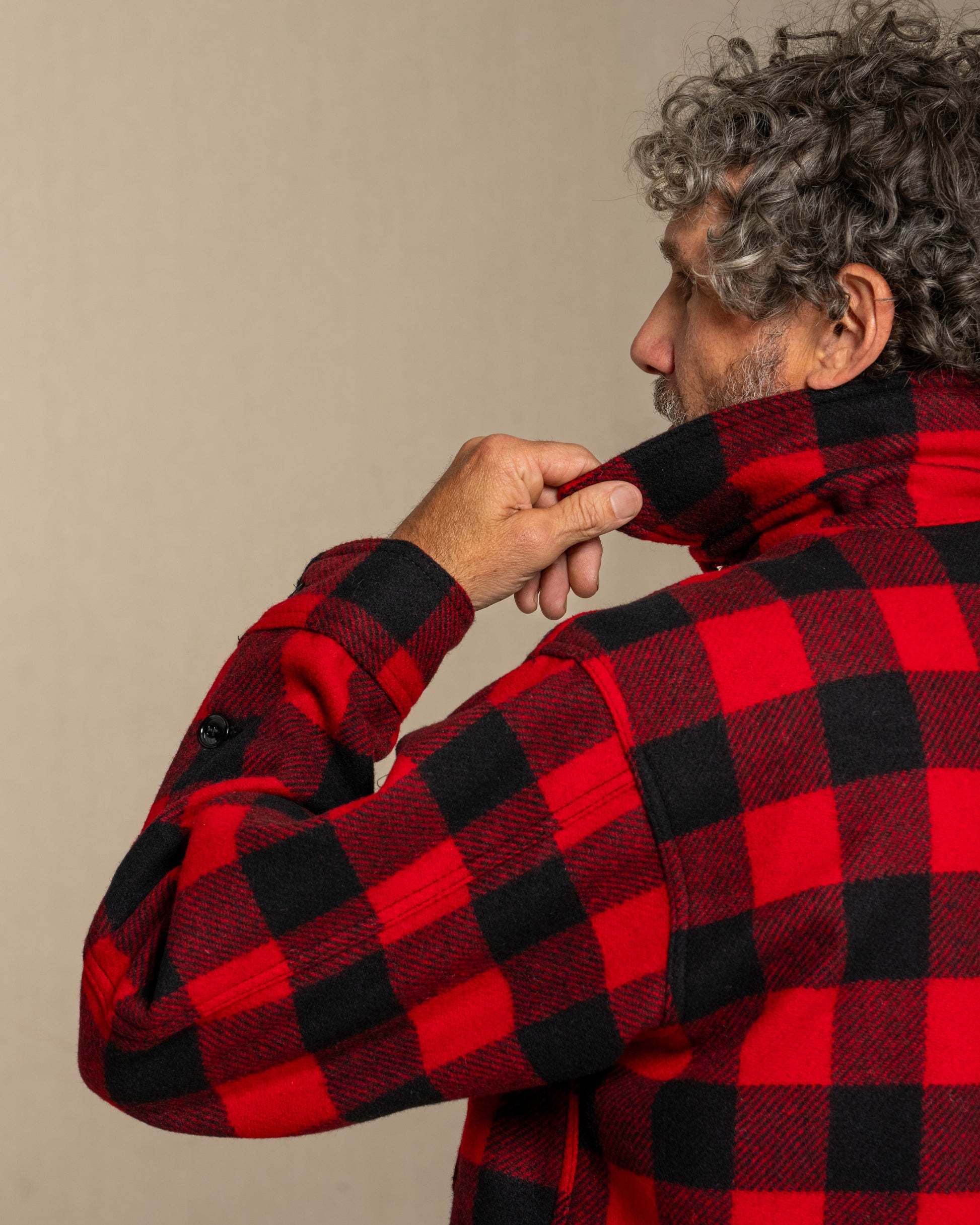 Man wearing a red and black checkered wool shirt against a beige background