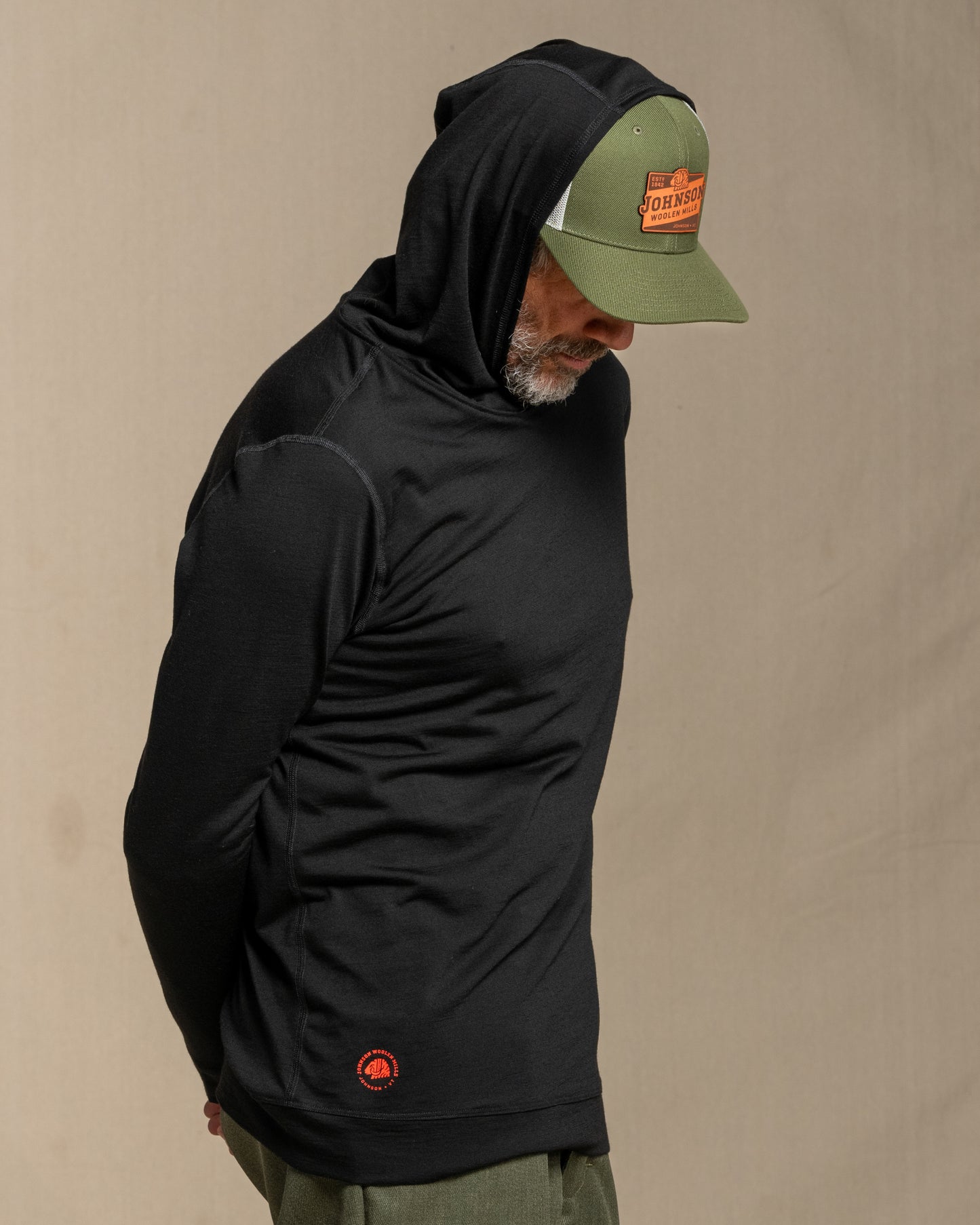 Man wearing a black merino wool hoodie against a beige background