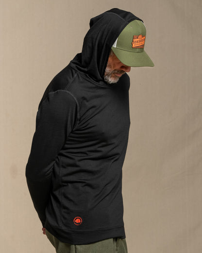 Man wearing a black merino wool hoodie against a beige background