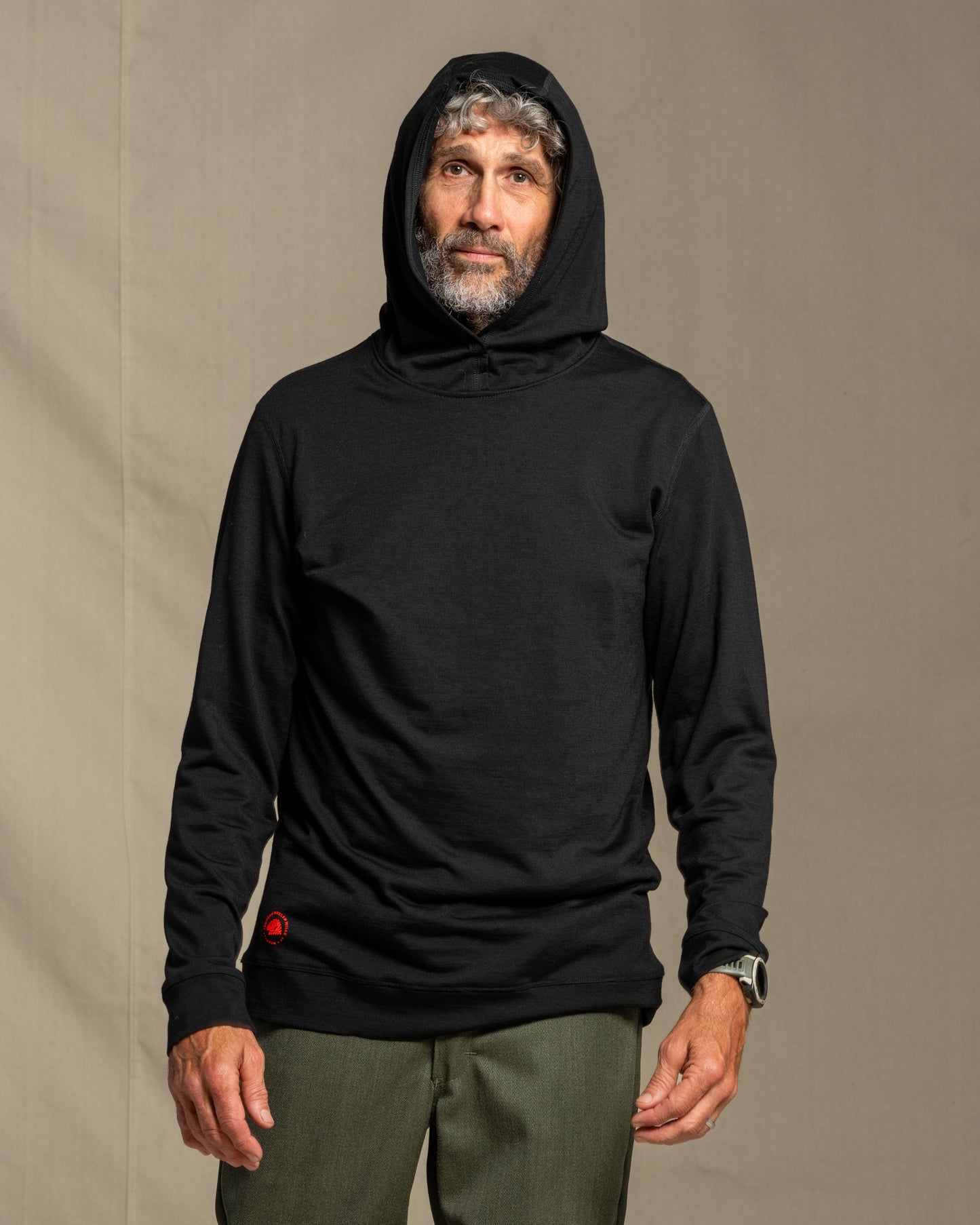 Man wearing a black merino wool hoodie against a beige background
