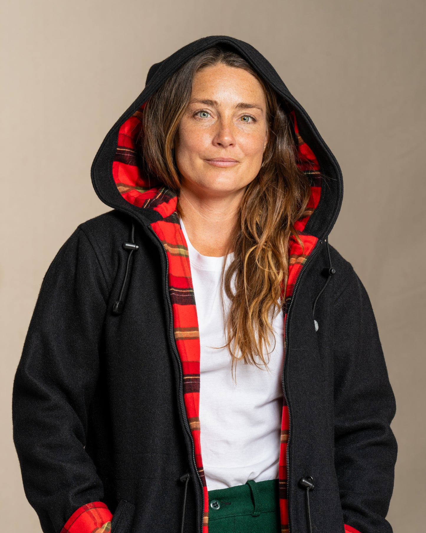 Person wearing a black wool coat with a red plaid flannel lining on a beige background