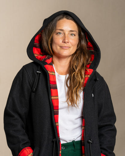 Person wearing a black wool coat with a red plaid flannel lining on a beige background