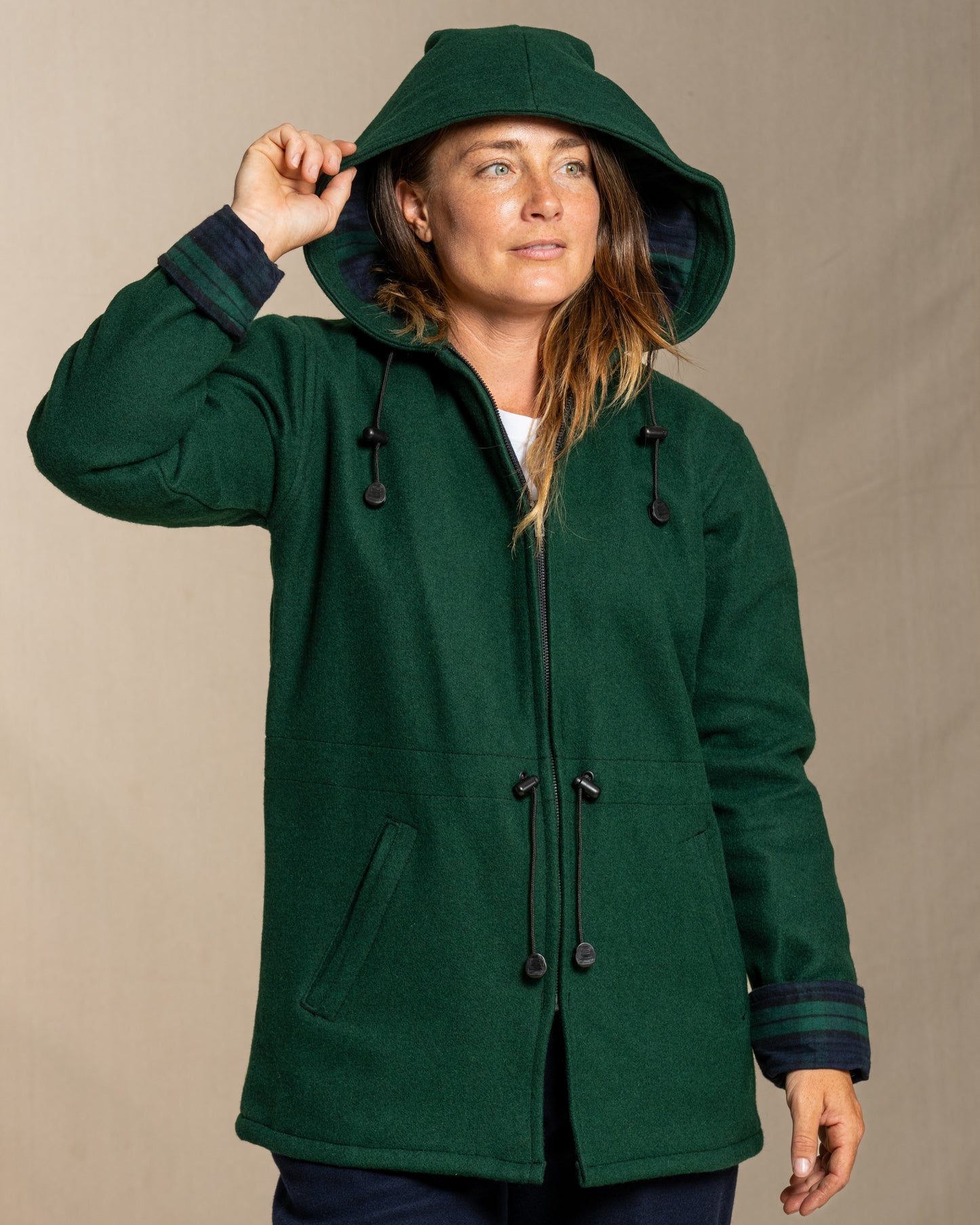 Woman wearing a green wool coat with a hood against a beige background