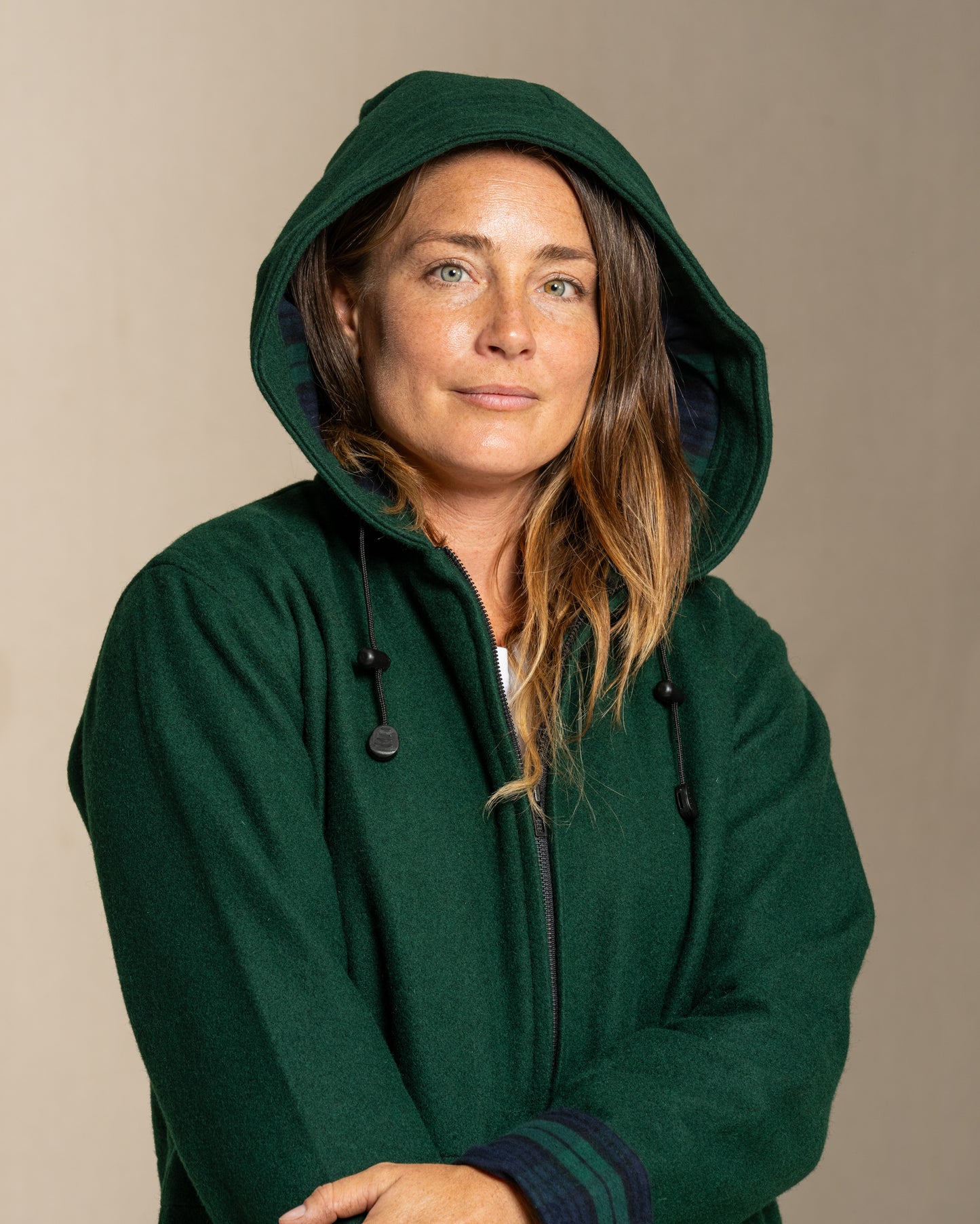 Person wearing a green hooded wool coat against a beige background