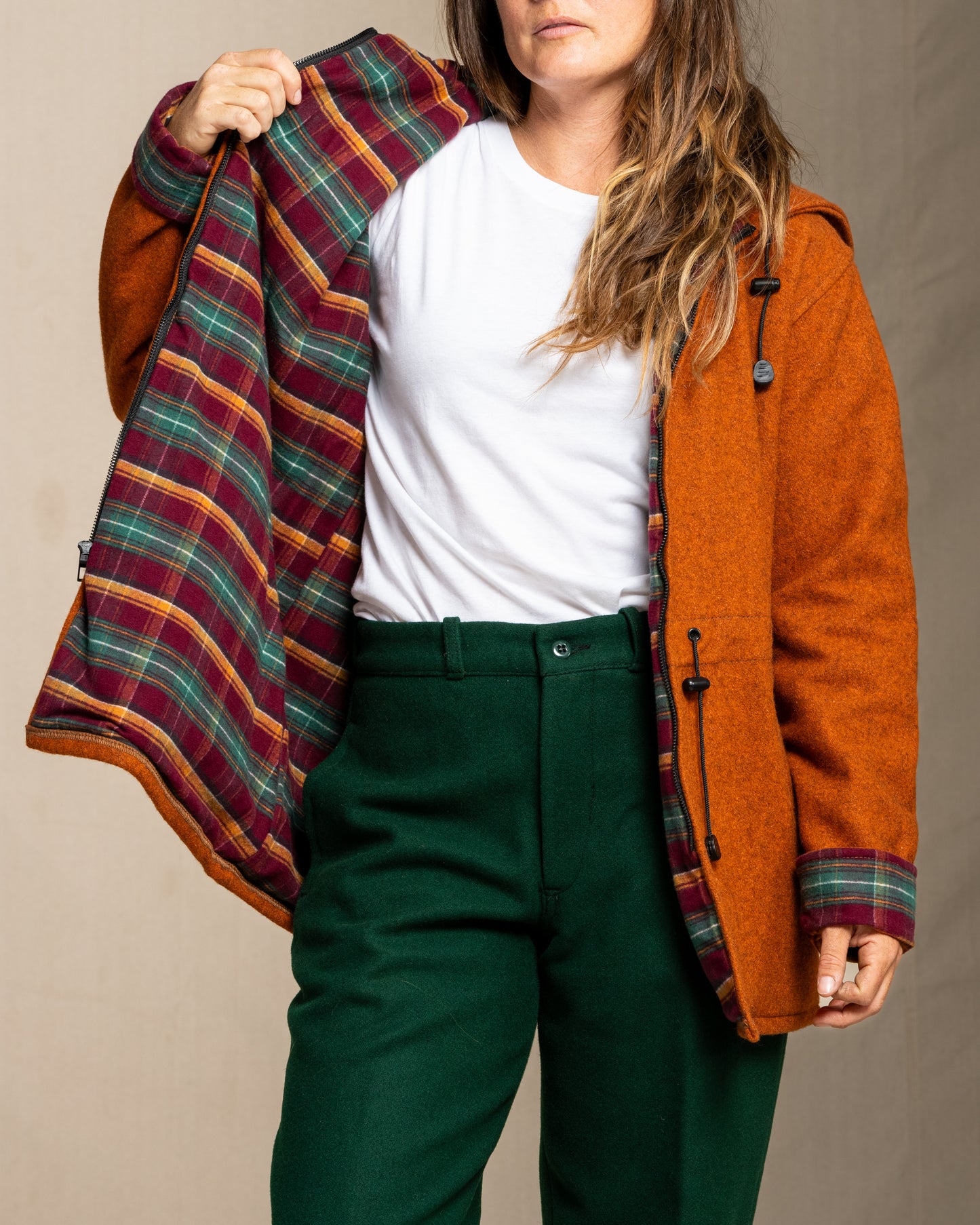 Person wearing a plaid jacket over an orange coat with a plain background