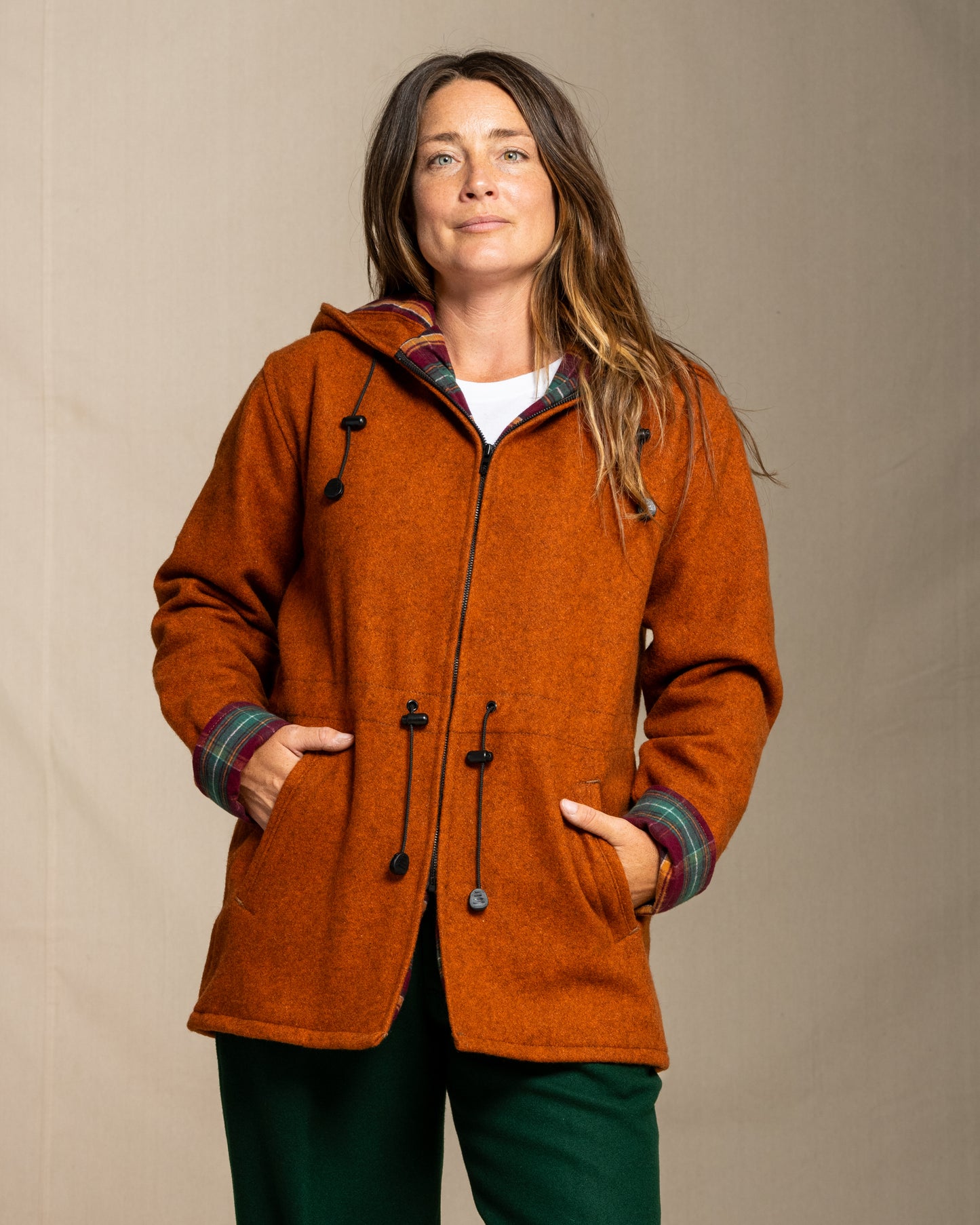 Woman wearing a orange coat with a plaid hood against a beige background