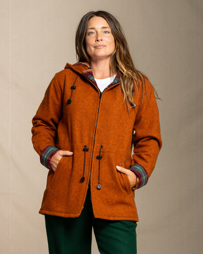 Woman wearing a orange coat with a plaid hood against a beige background