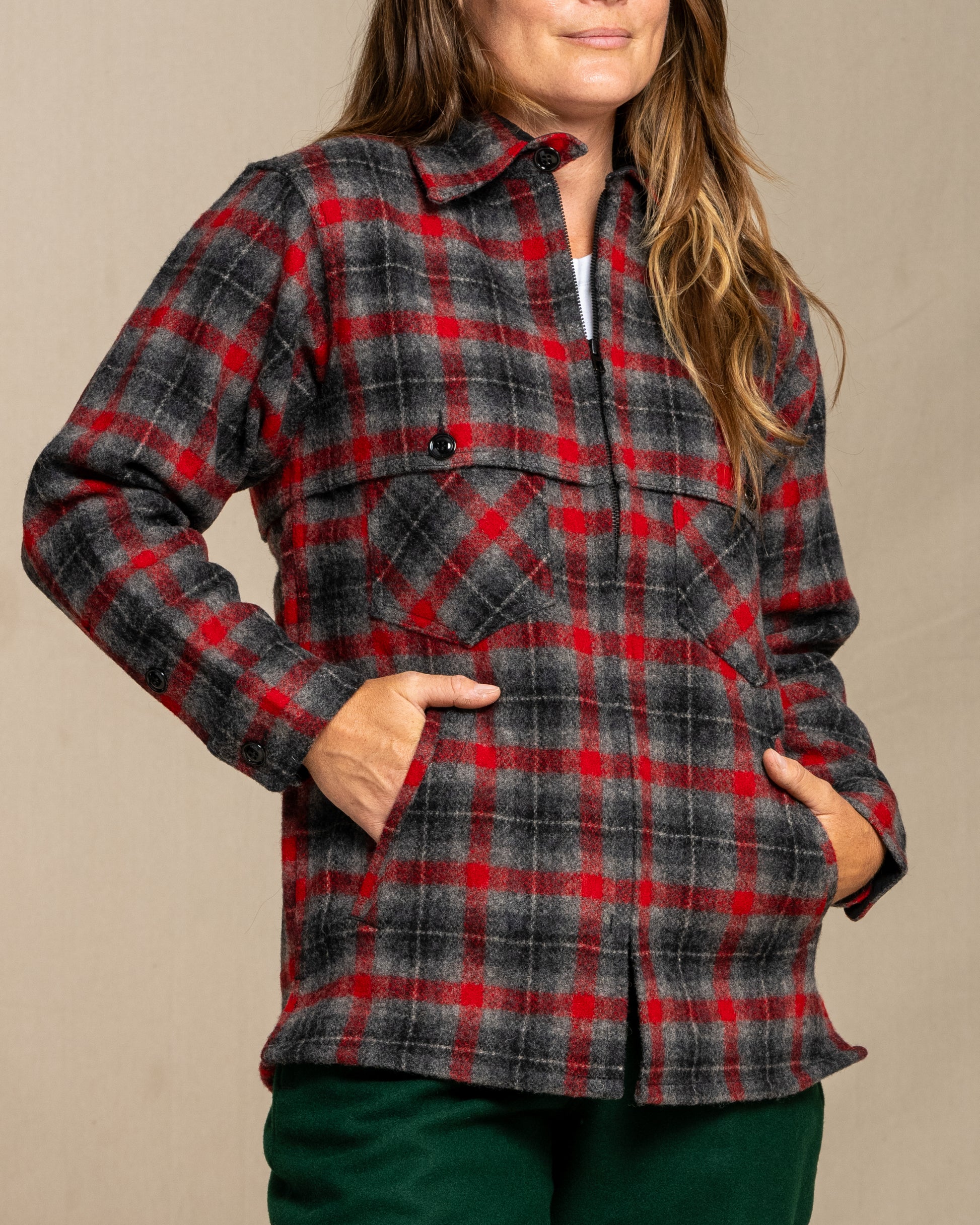 Person wearing a wool red and gray plaid jacket and green wool pants against a beige background