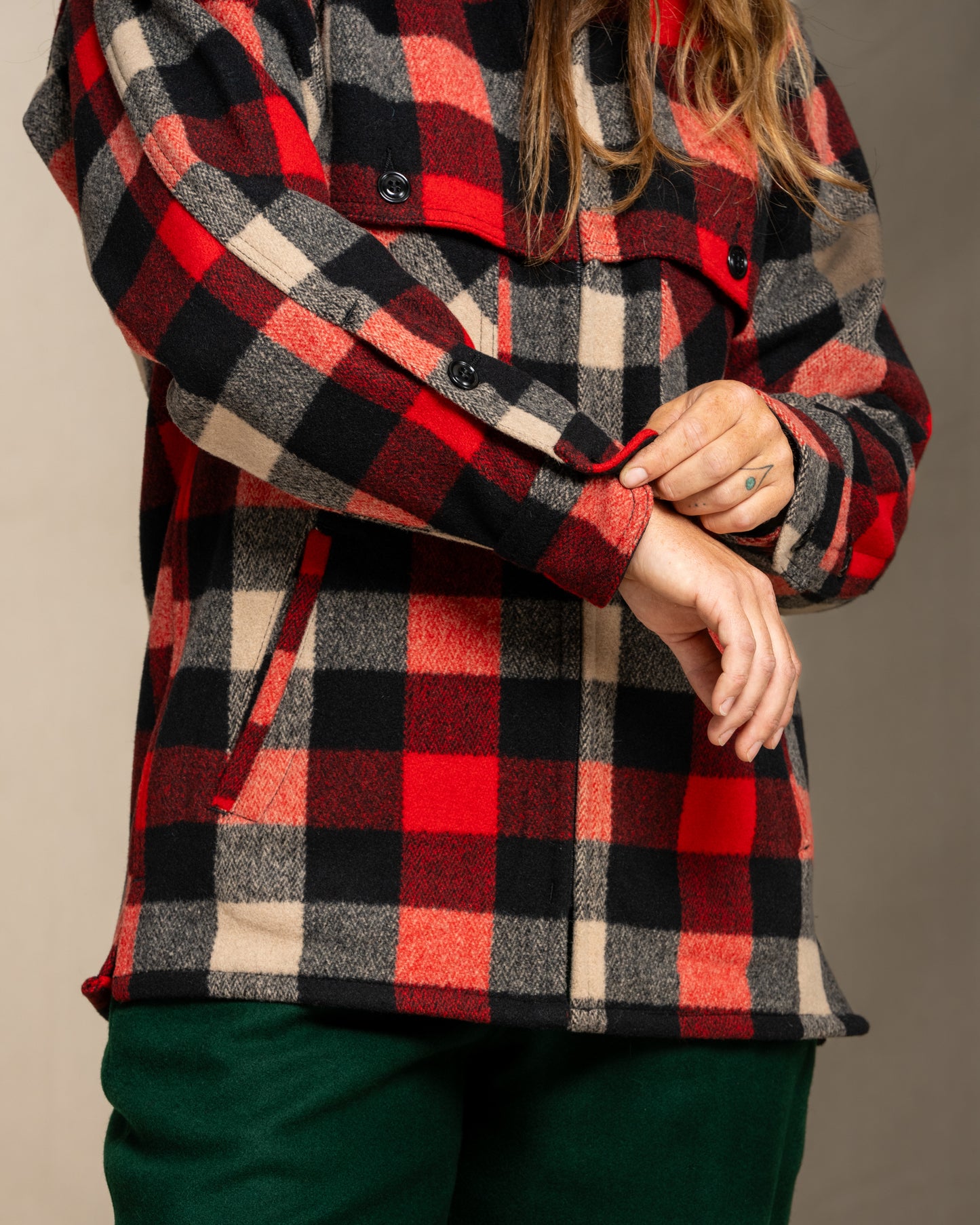 Person wearing a wool red and black and beige plaid jacket against a neutral background