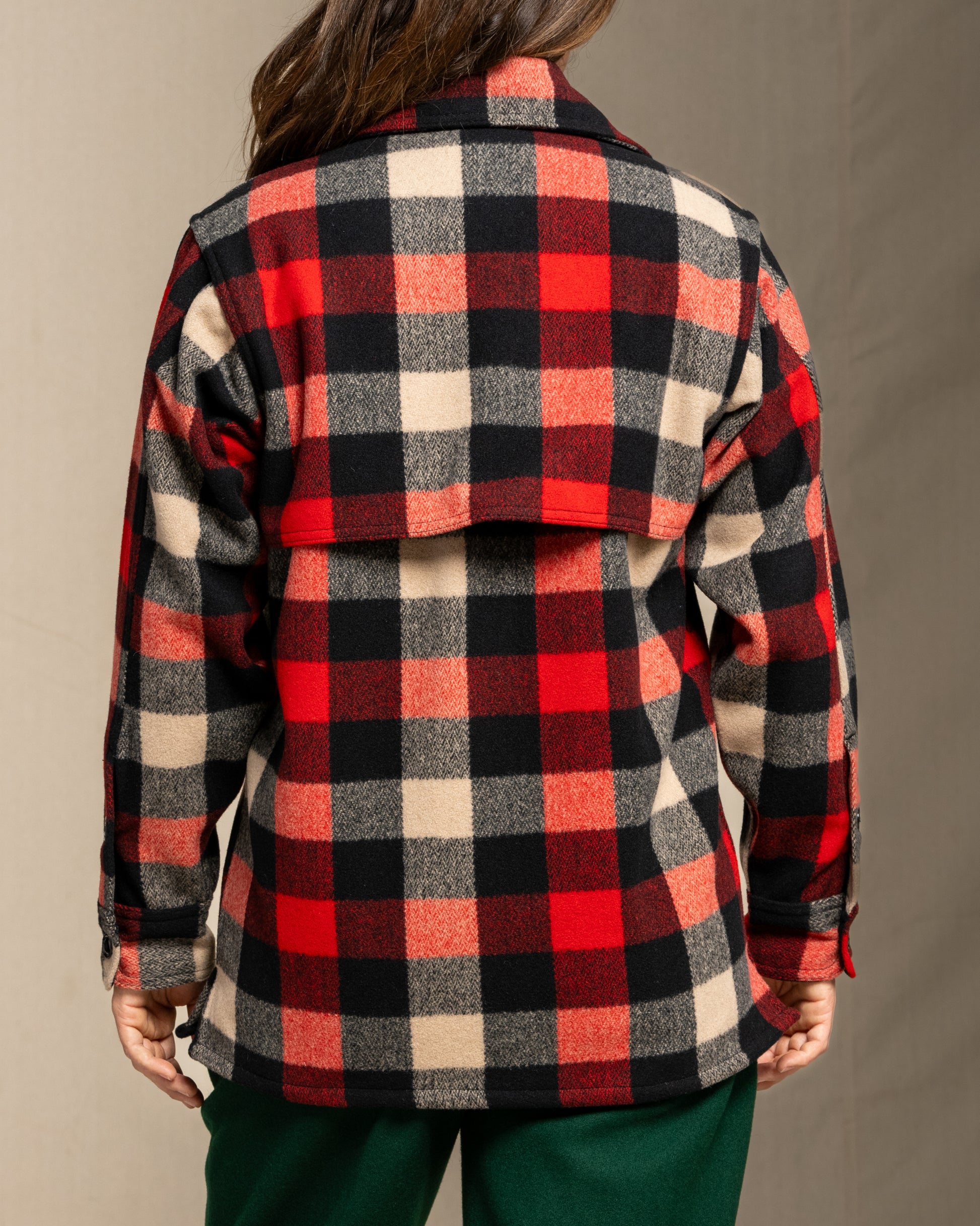 Person wearing a wool red and black and beige plaid jacket against a neutral background