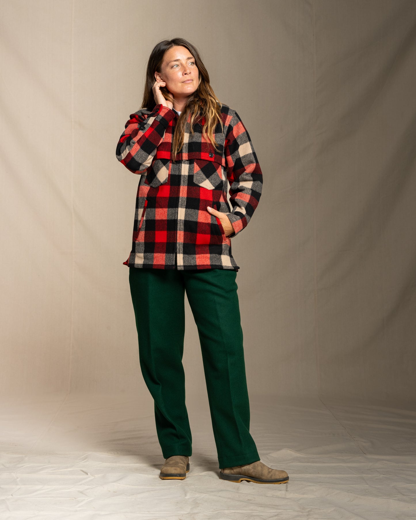 Person wearing a wool red and gray plaid jacket and green wool pants against a beige background
