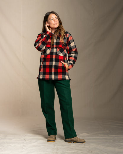 Person wearing a wool red and gray plaid jacket and green wool pants against a beige background
