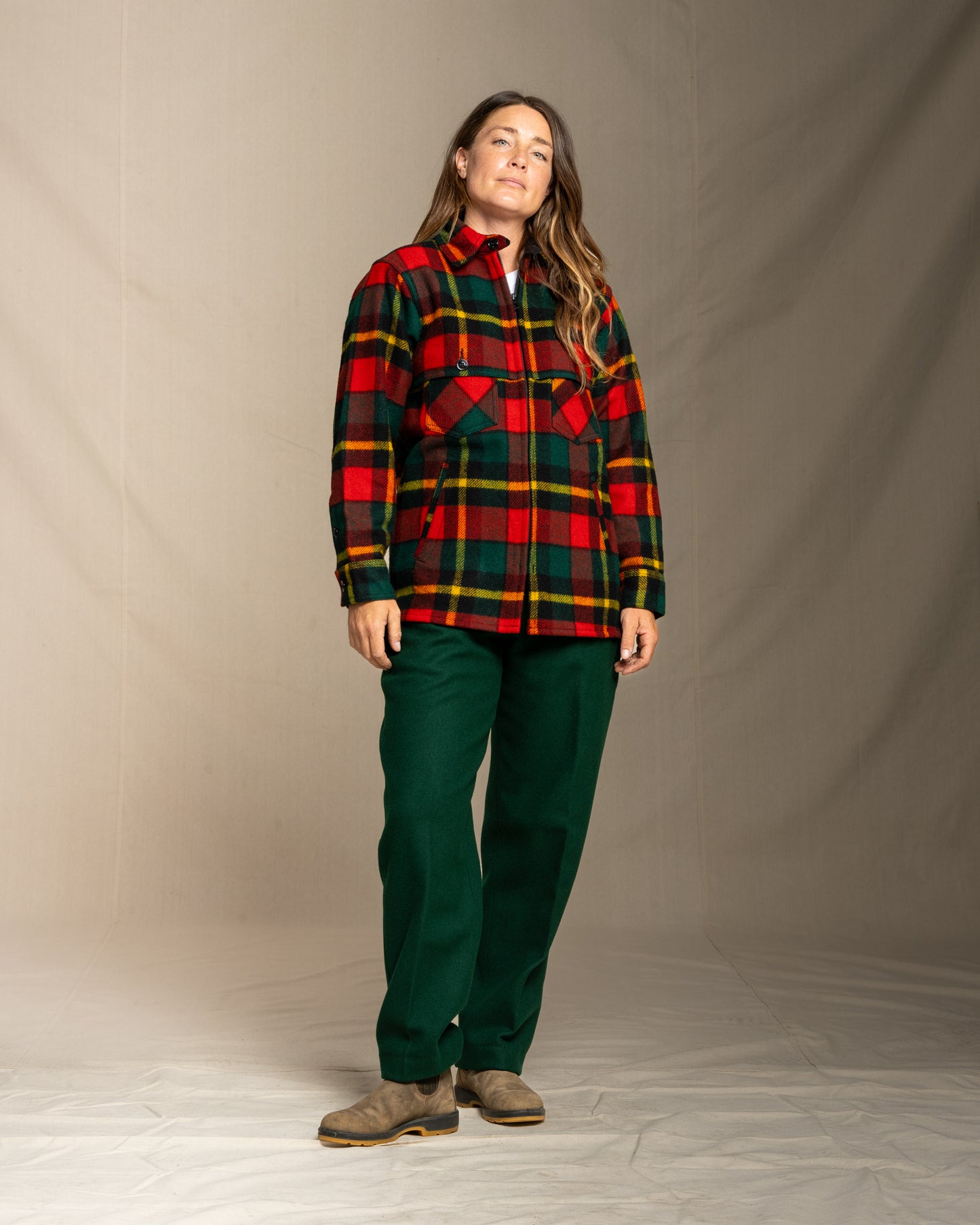 Person wearing a red yellow and green plaid wool jac shirt with wool green pants against a neutral background