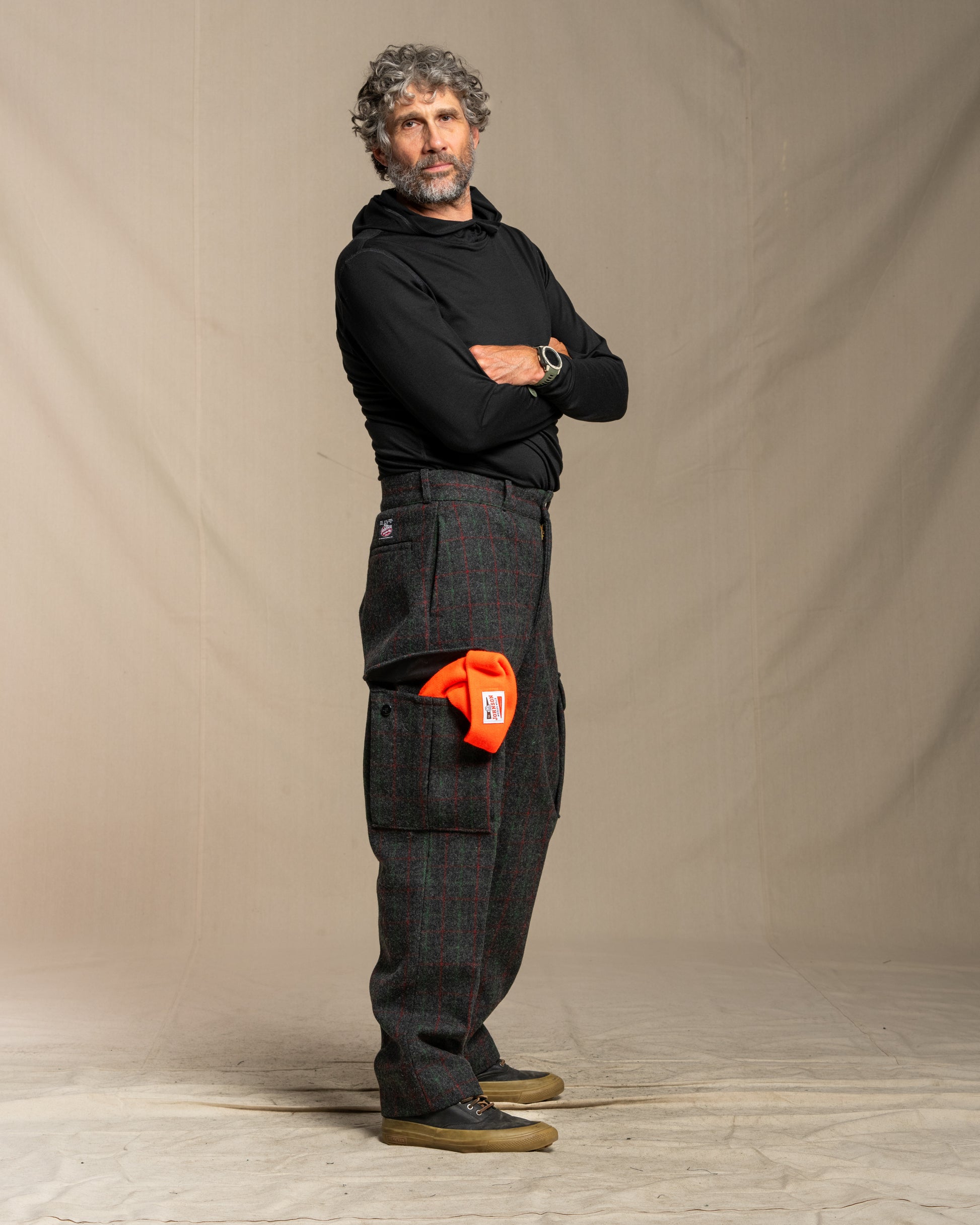 Man wearing black merino wool hoodie and wool cargo pants with an orange hat in pocket