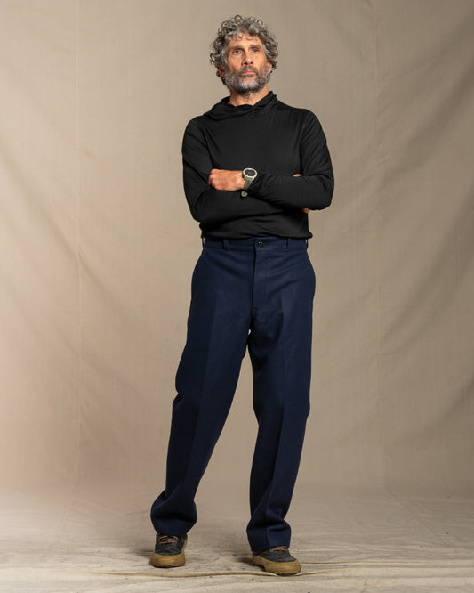 Man wearing a black hoodie and wool navy pants standing against a beige background