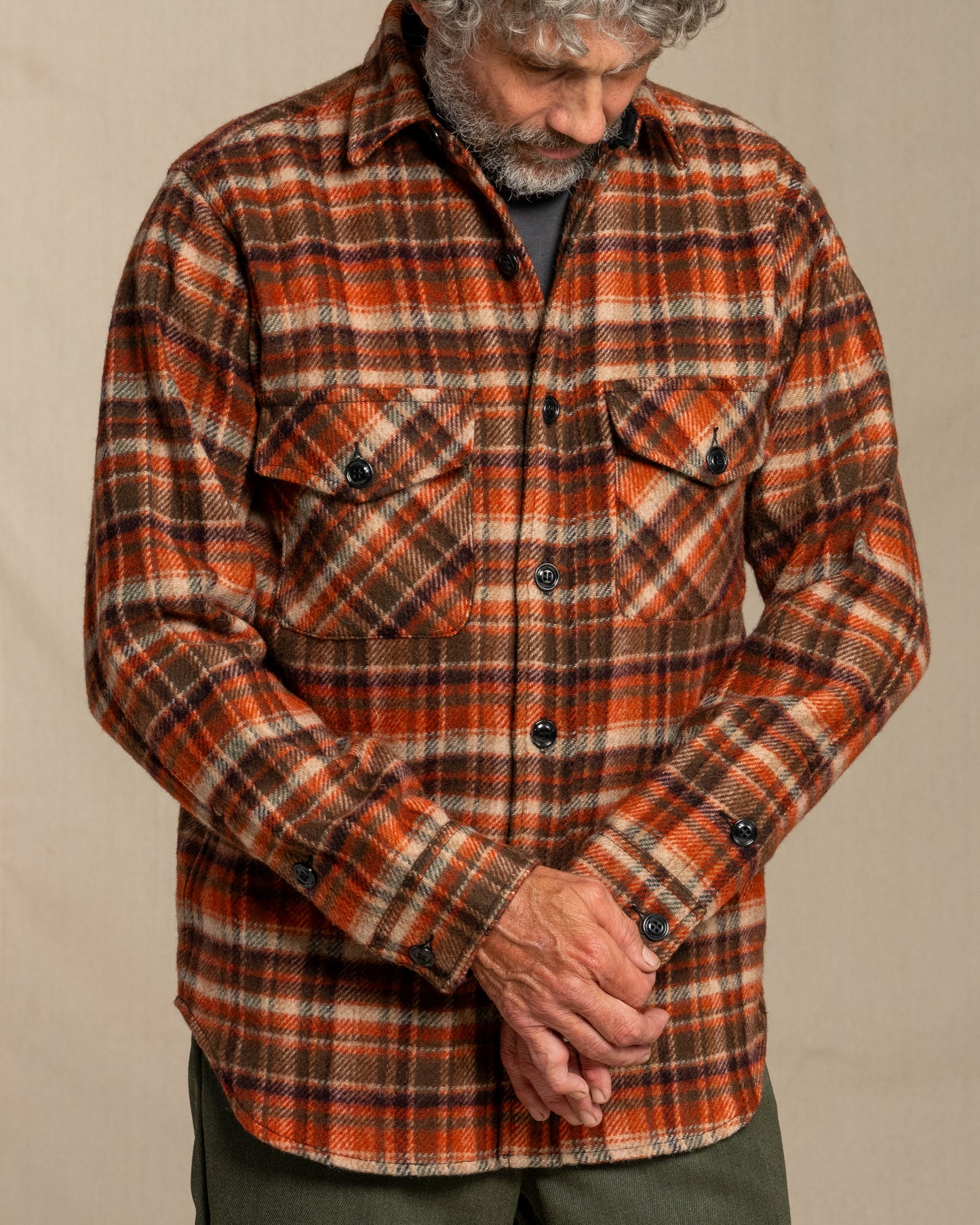 Man wearing a tan and brown plaid shirt against a beige background