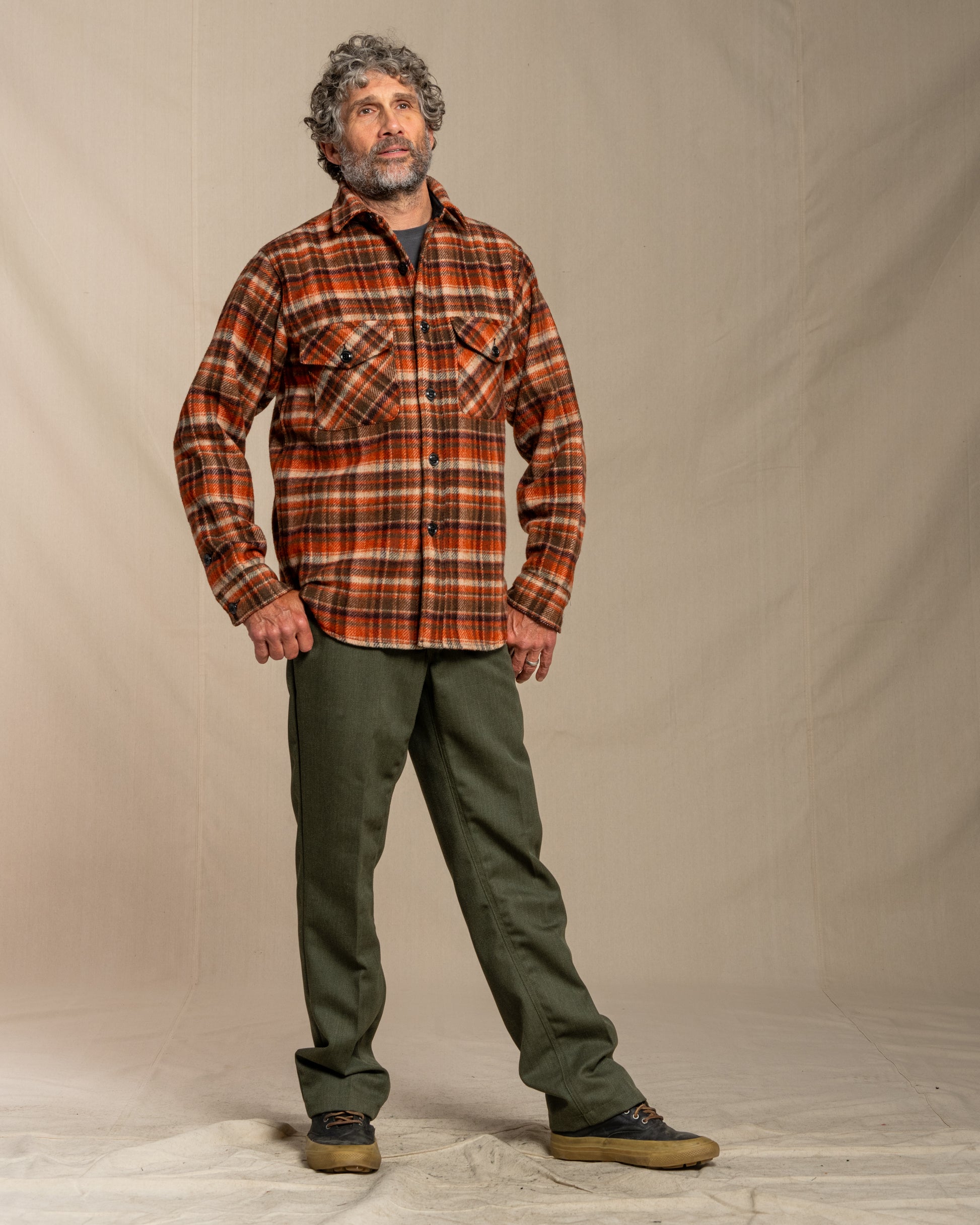 Man wearing a wool plaid shirt and green pants against a plain background