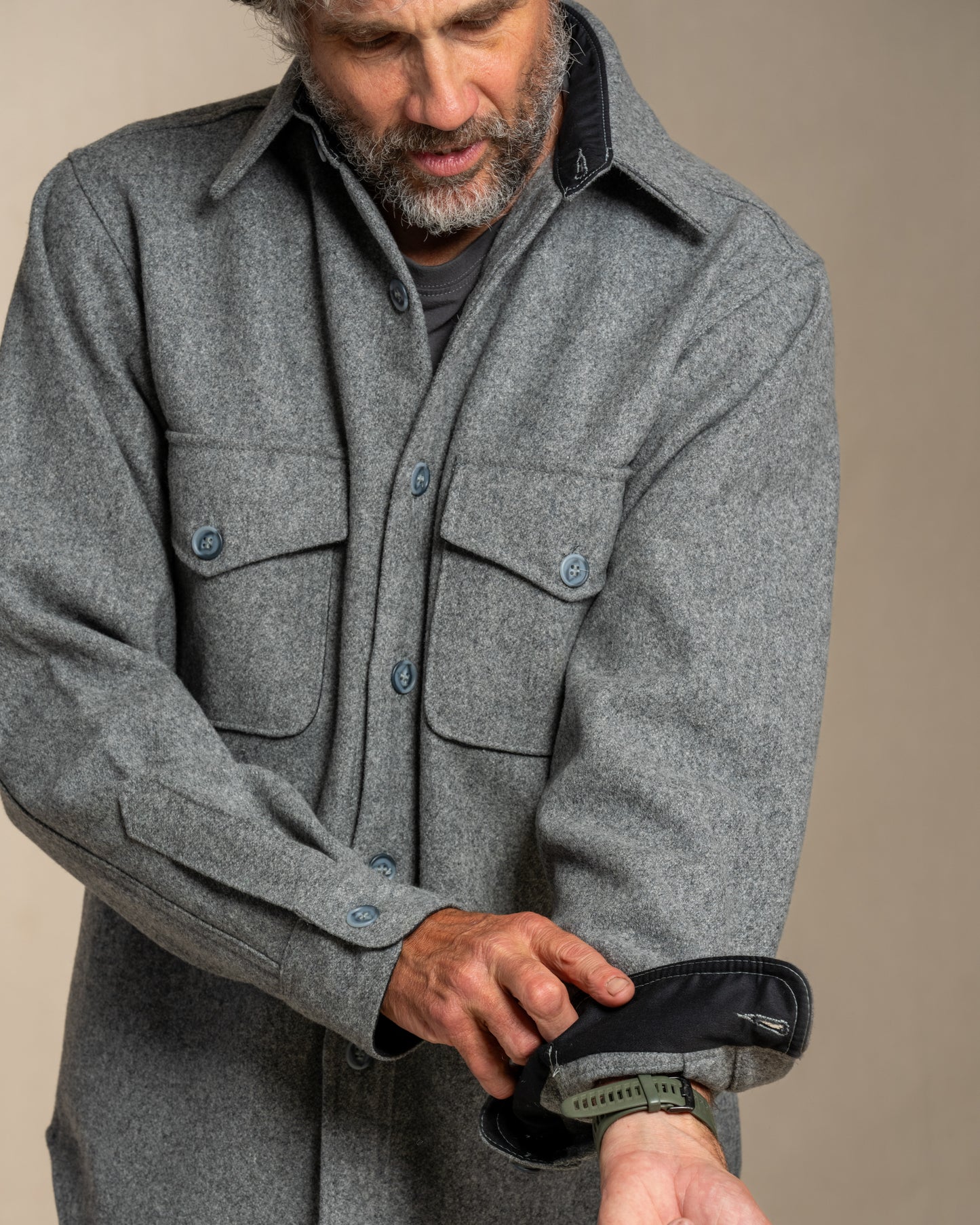 Man wearing a wool gray shirt rolling cuff against a beige background