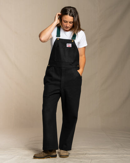 Person wearing wool black overalls with a beige background