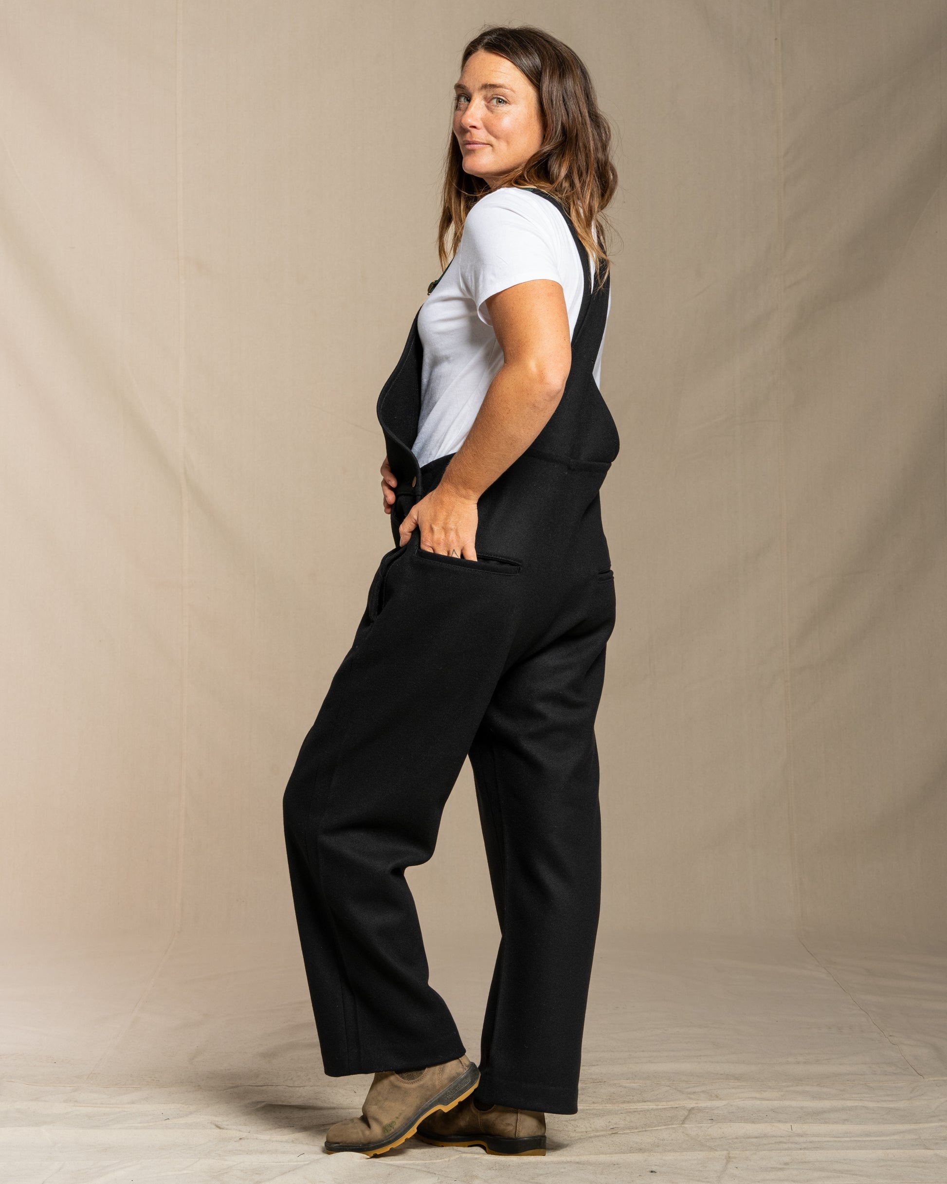 Woman wearing wool black overalls and a white shirt against a plain background