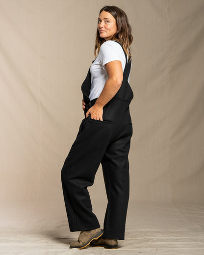 Woman wearing wool black overalls and a white shirt against a plain background
