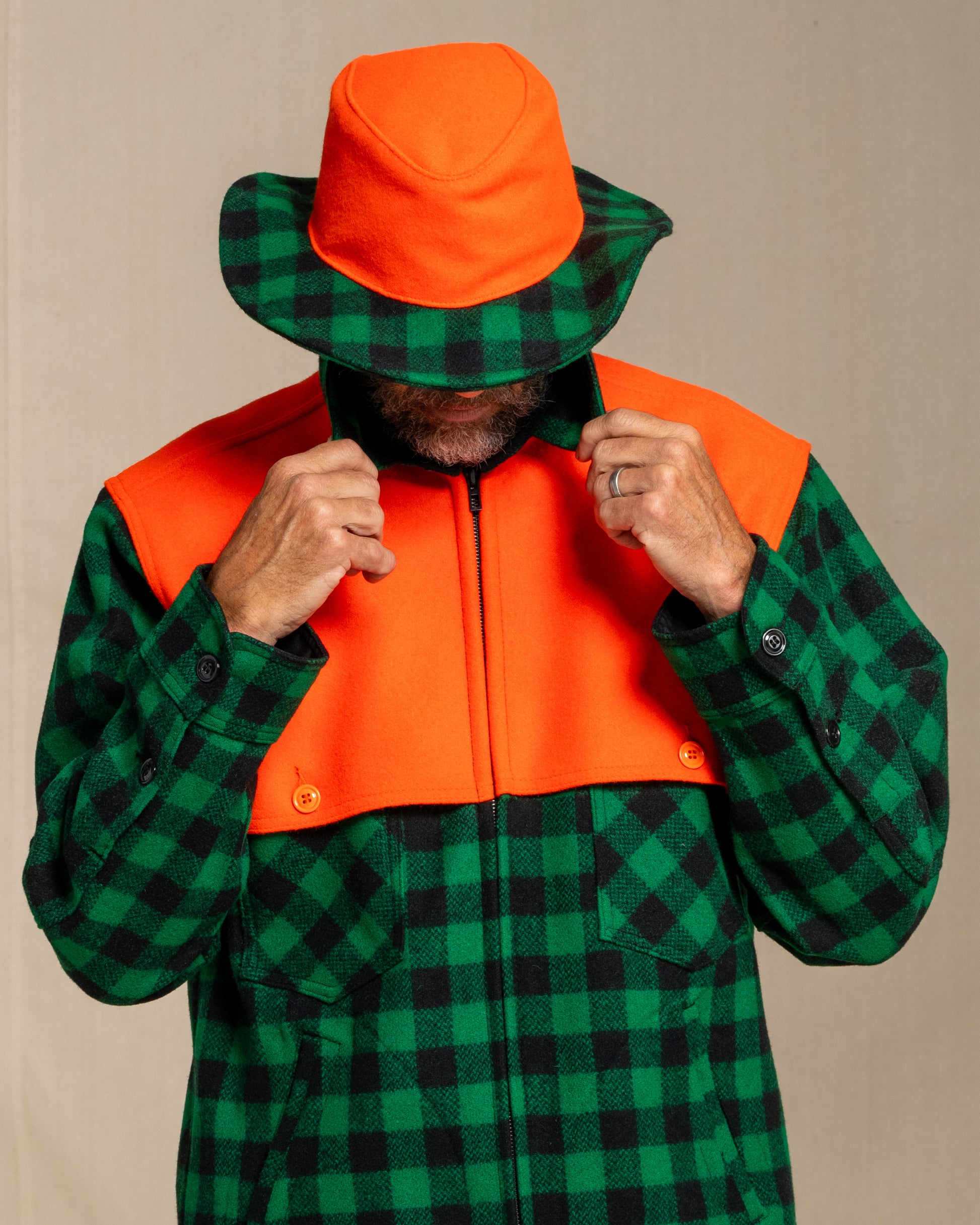 Person wearing a green and black checkered jacket with an orange cape against a canvas background