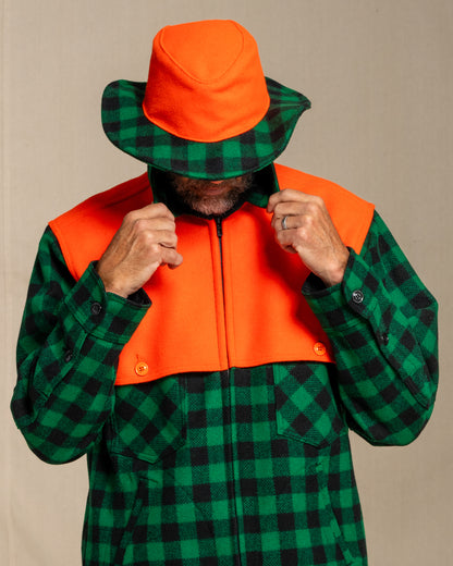 Person wearing a green and black checkered jacket with an orange cape against a canvas background