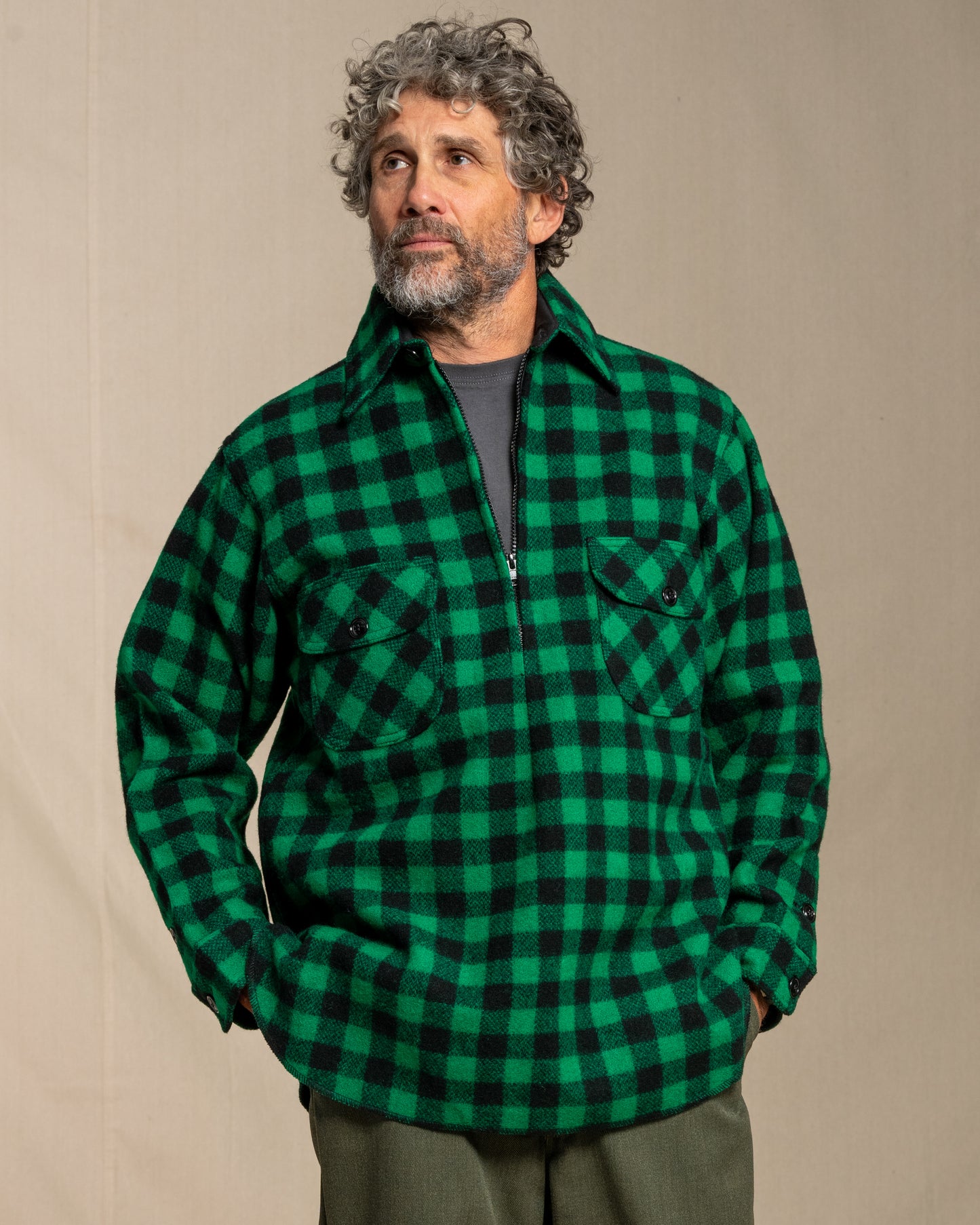 Man wearing a green and black checkered half zip wool shirt against a beige background