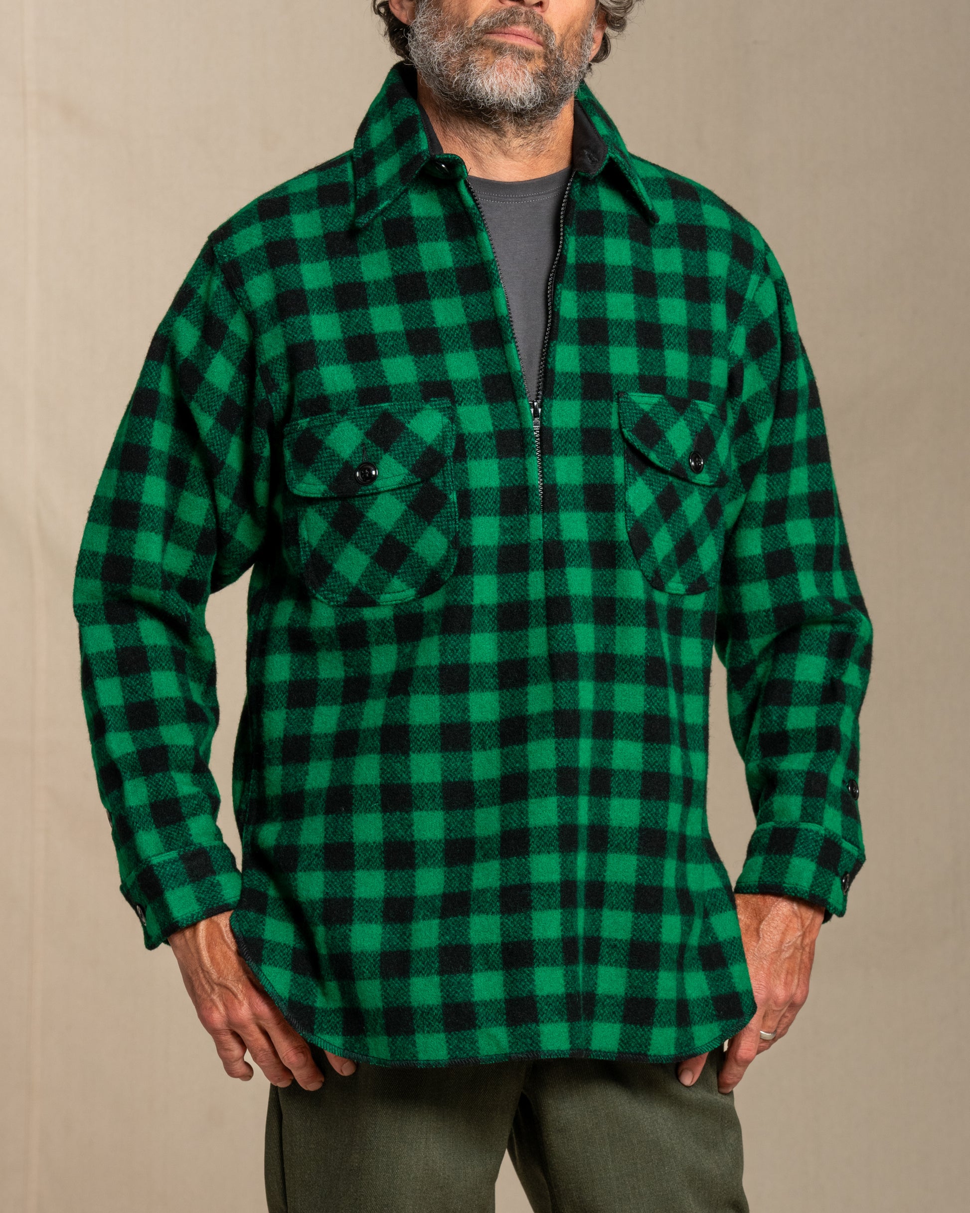 Man wearing a green and black checkered half zip wool shirt against a beige background