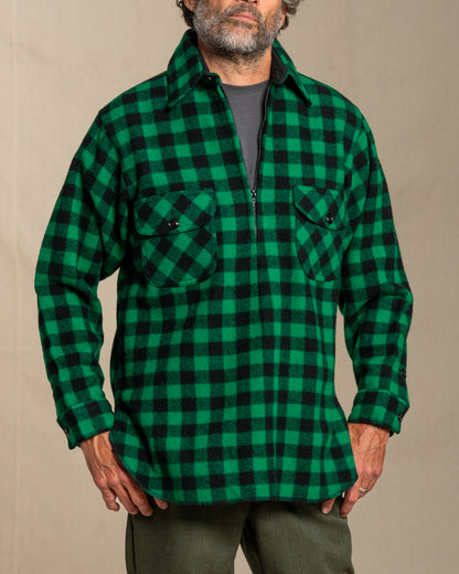 Man wearing a green and black checkered half zip wool shirt against a beige background