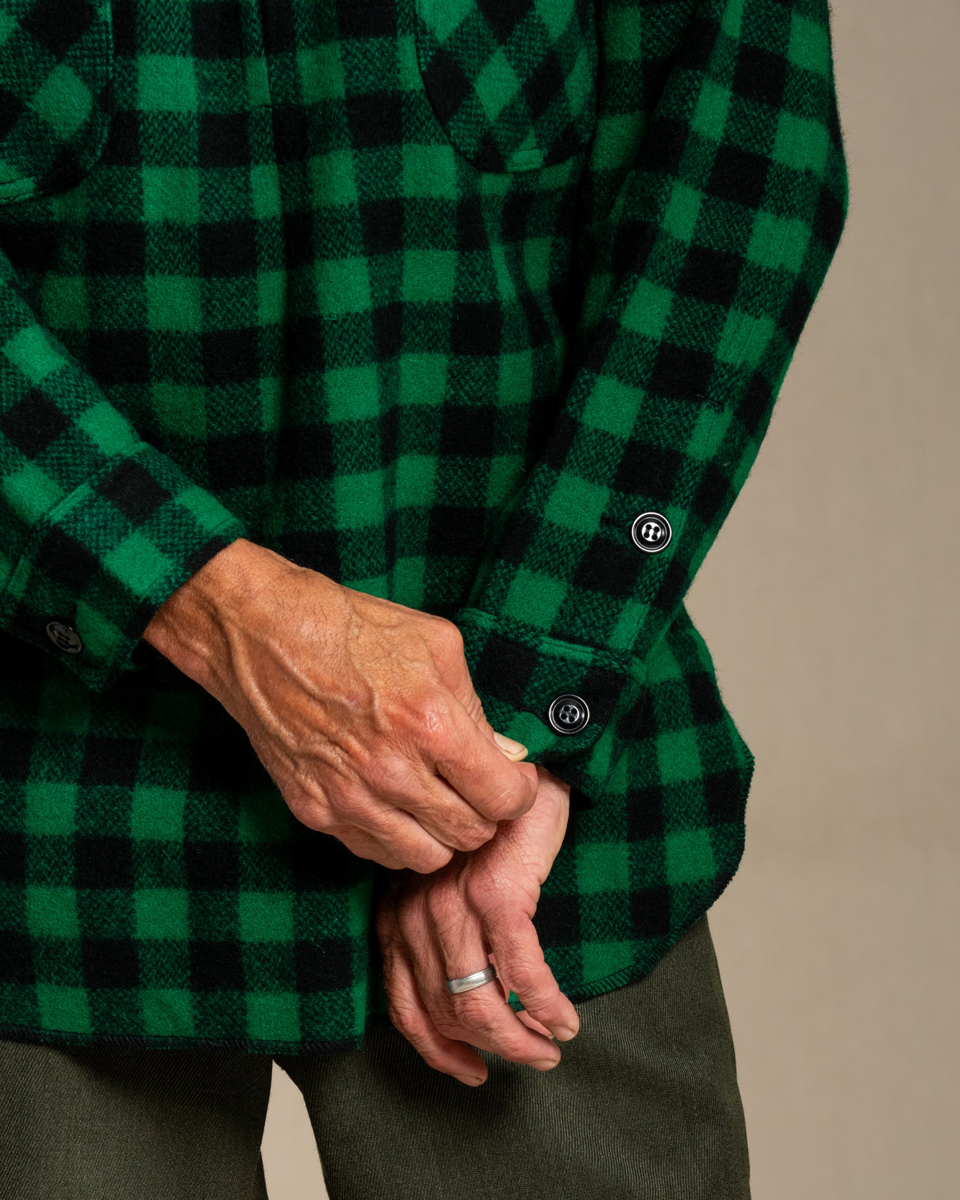 Green and black checkered shirt with a close-up of hands wearing a ring.