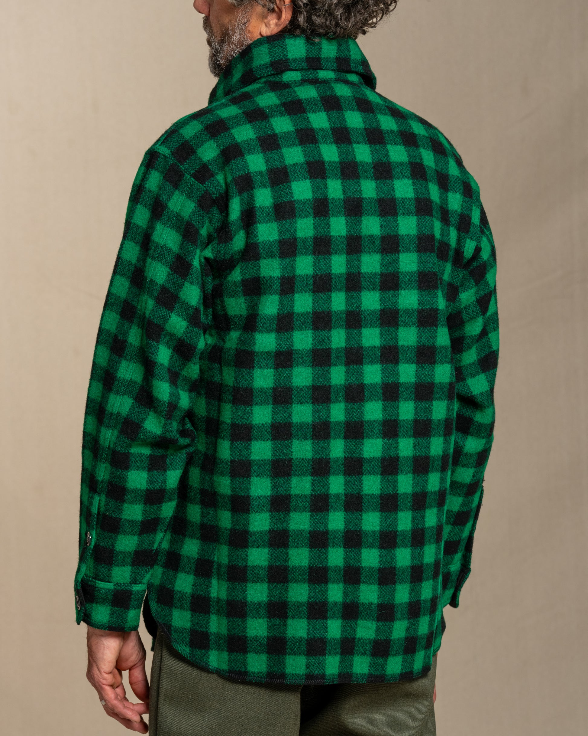 Person wearing a green and black checkered shirt against a beige background